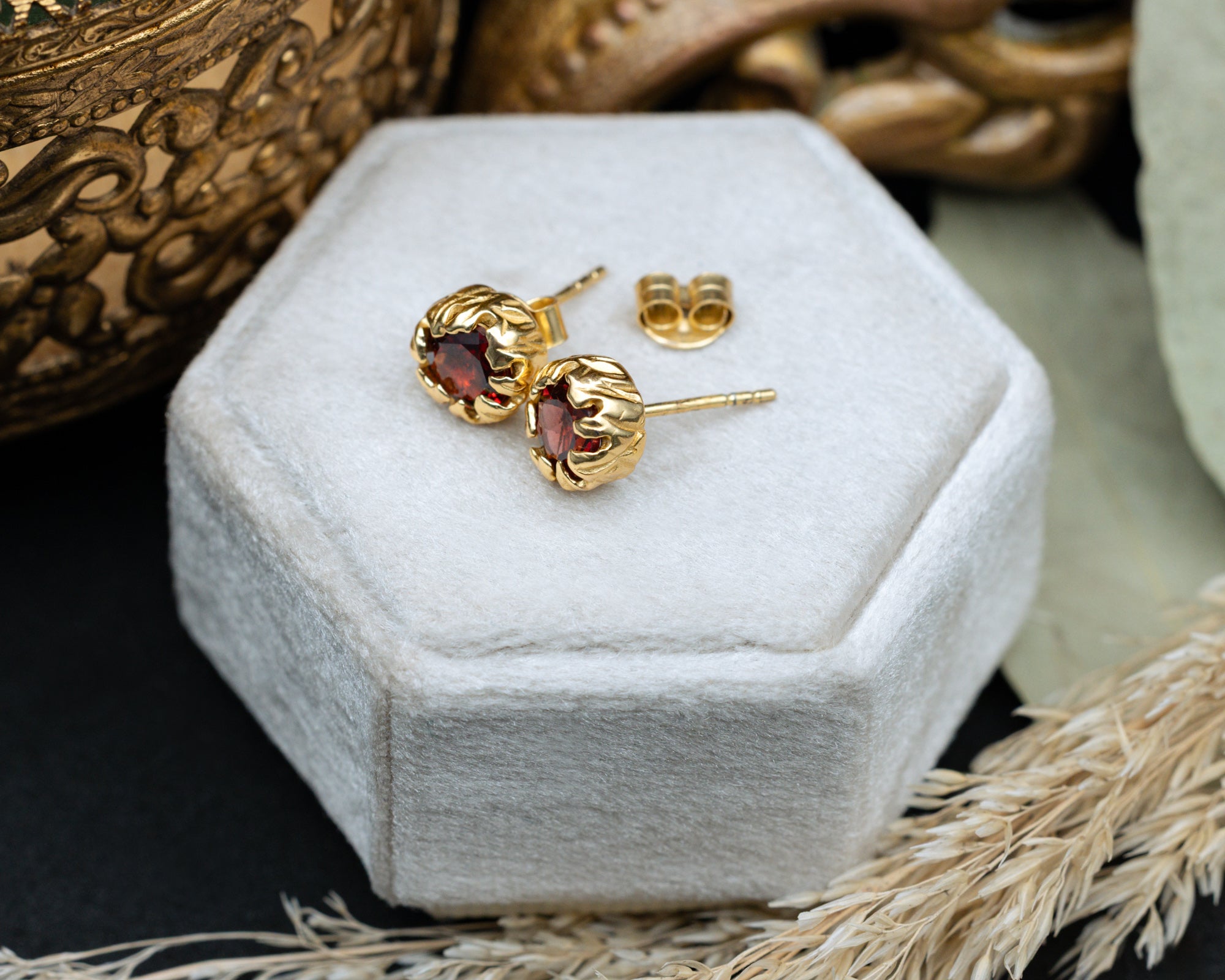 Gold earrings with red garnets on a white hexagonal jewelry box.