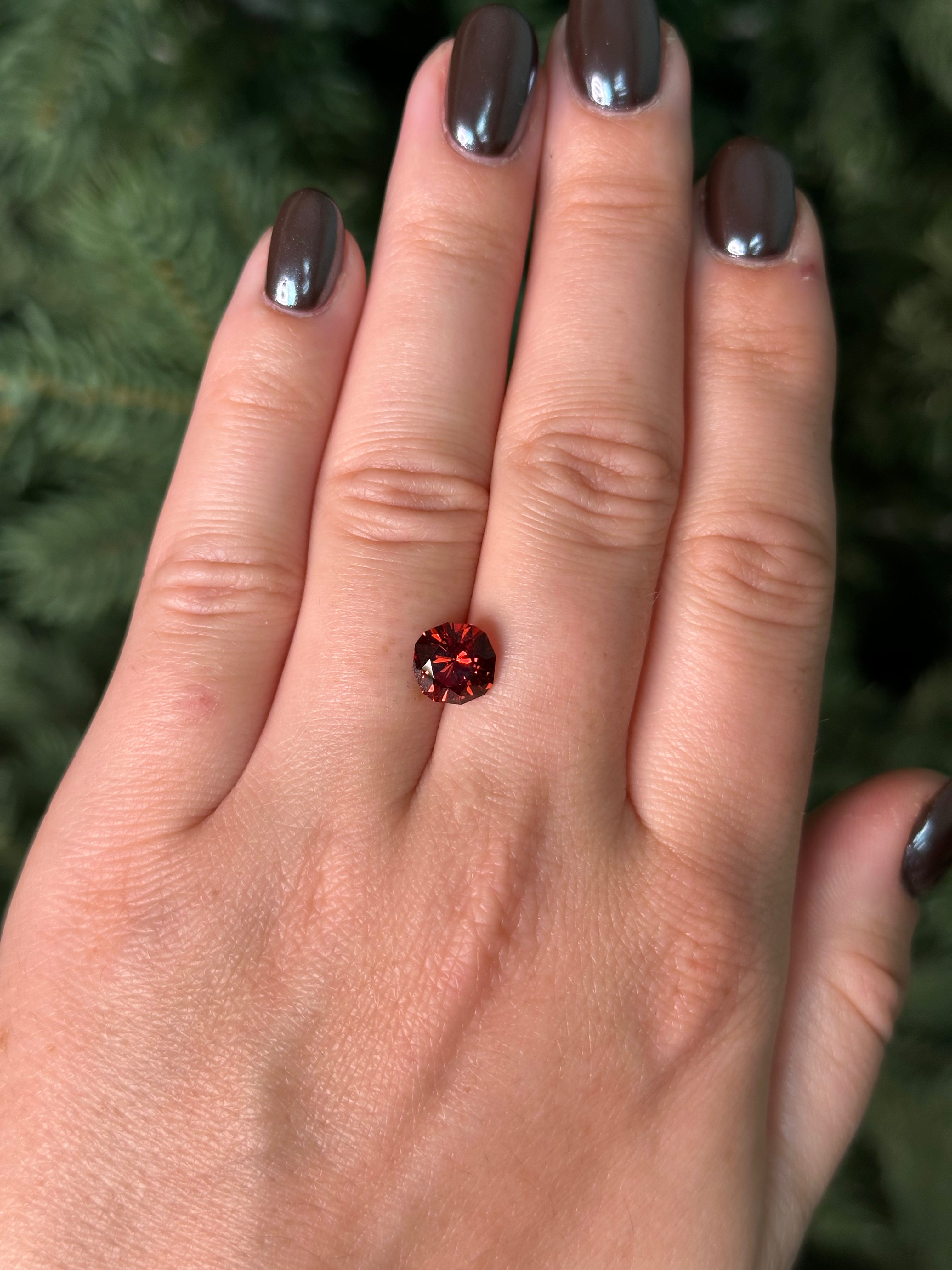 Hand with a red garnet sitting on fingers against a blurred green background