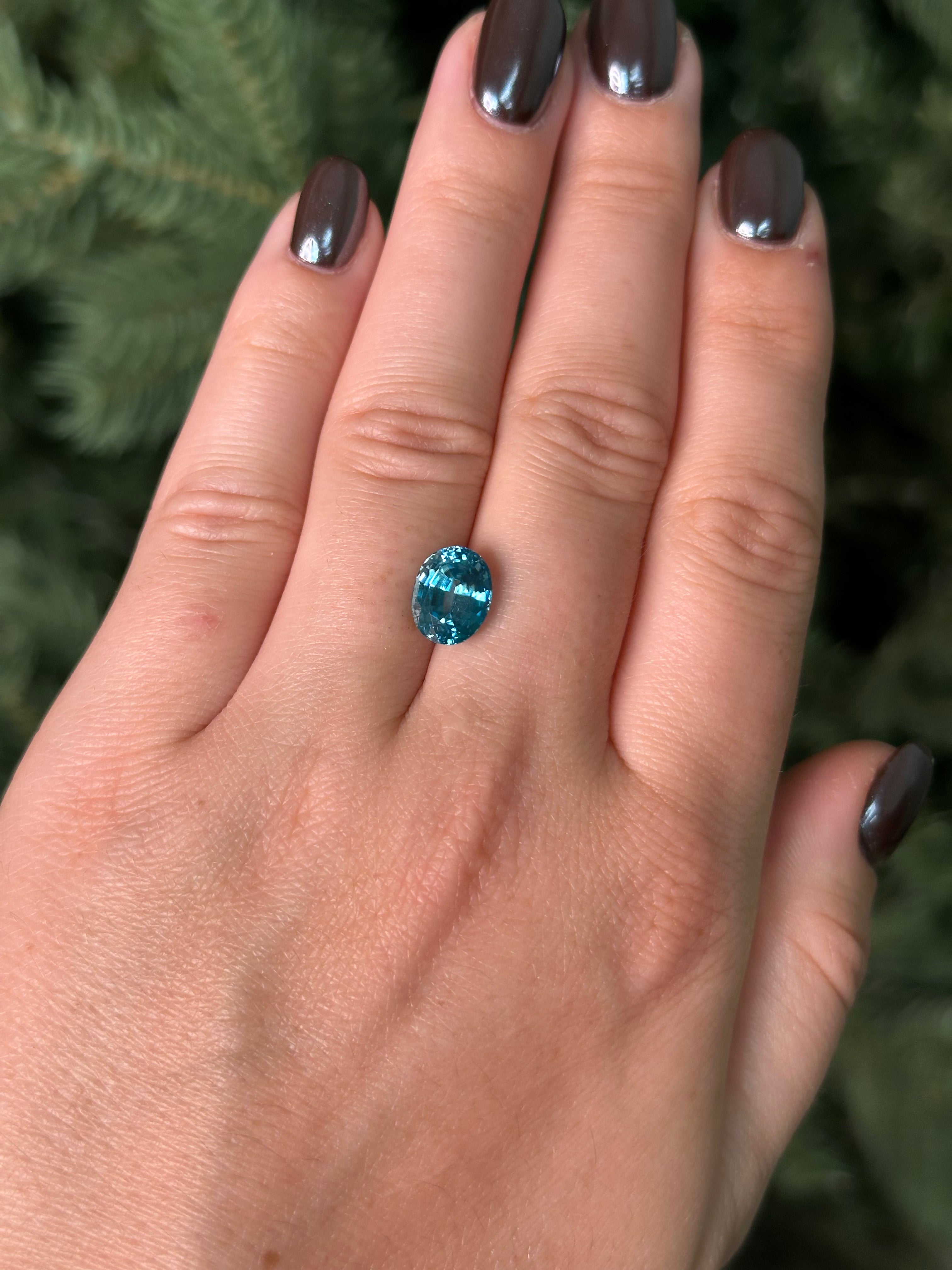 Hand with a blue zircon sitting on fingers against a blurred green background