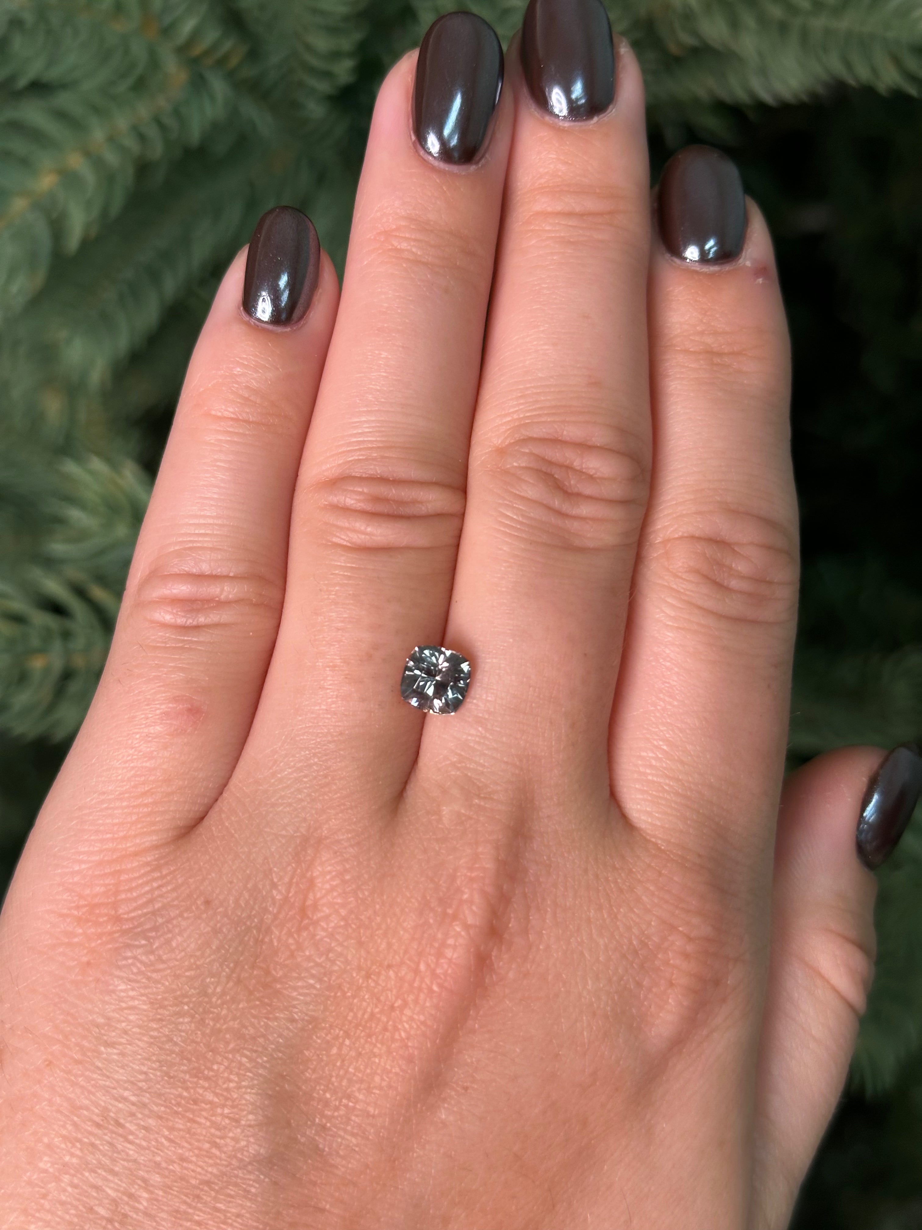 Hand with a silver sapphire sitting on fingers against a blurred green background