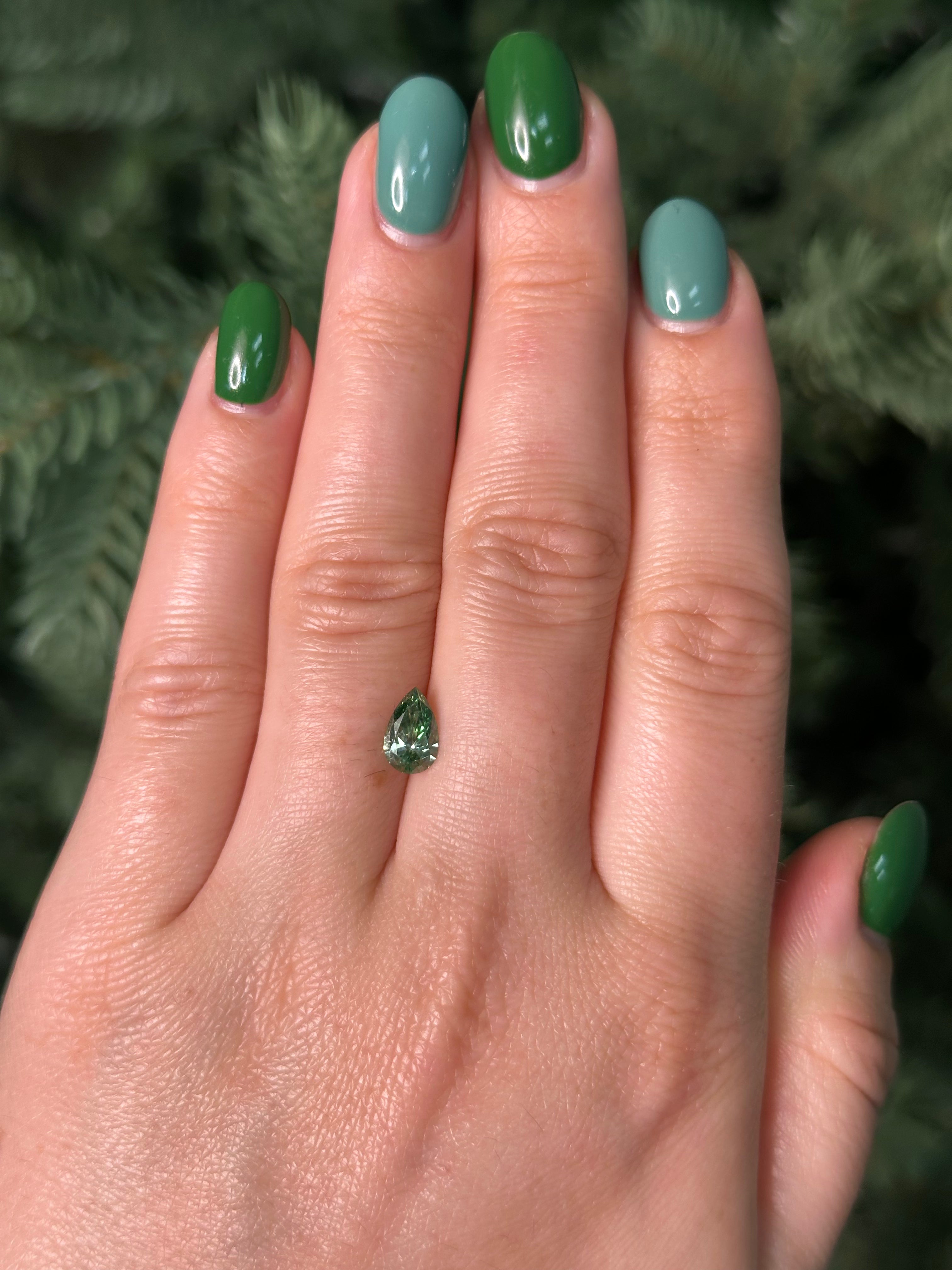 Hand with green nail polish holding a small green gemstone against a blurred natural background