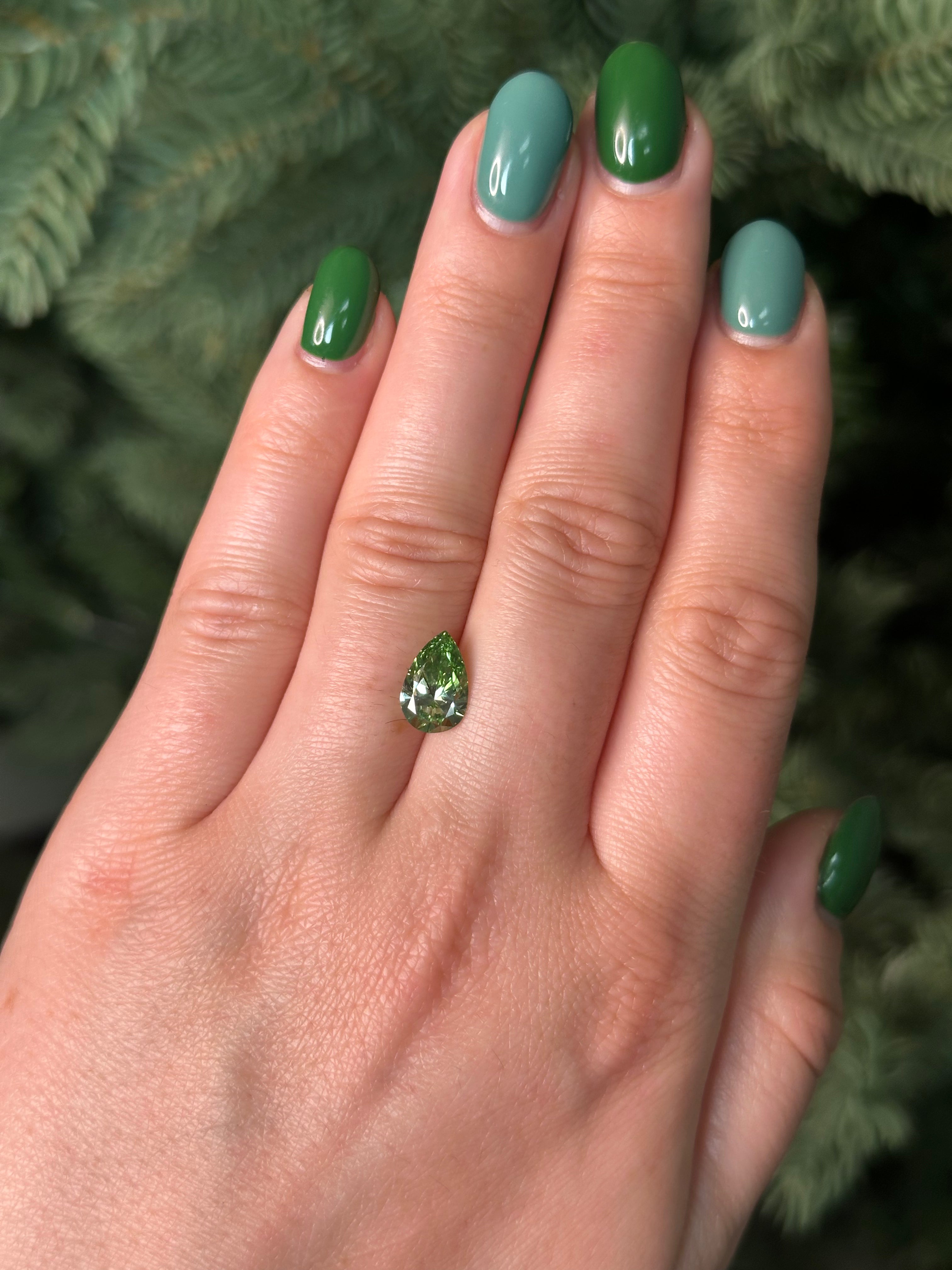 Hand with green nail polish holding a green diamond against a blurred natural background