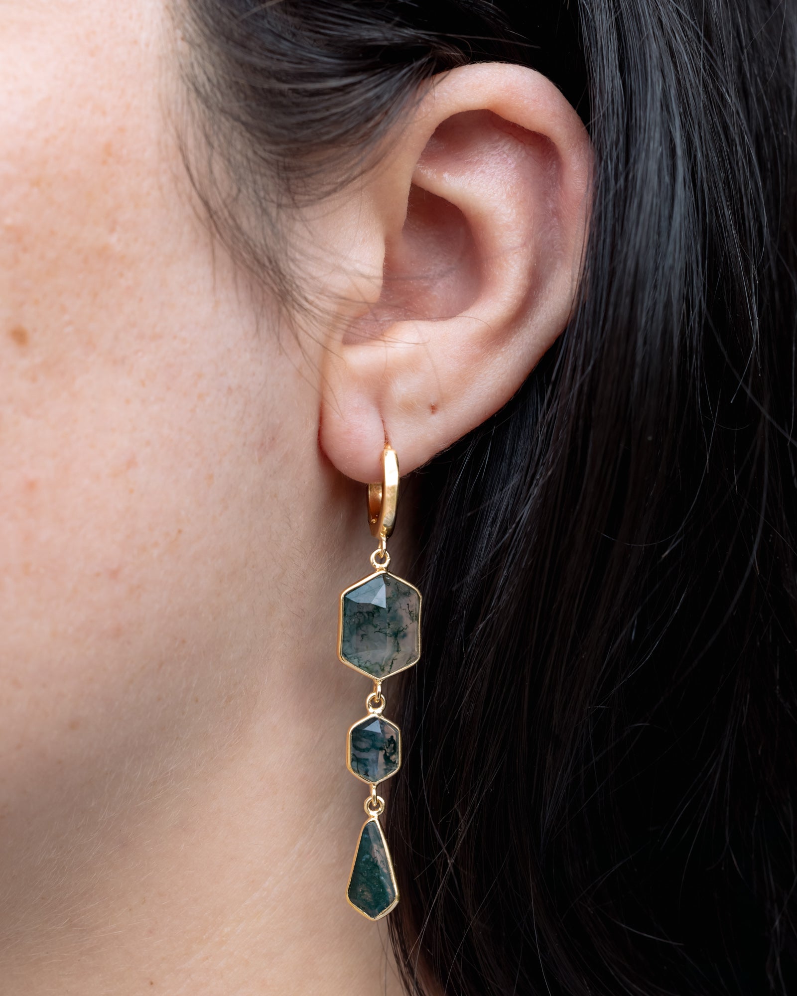 Close-up of an ear wearing a gold earring with moss agate.