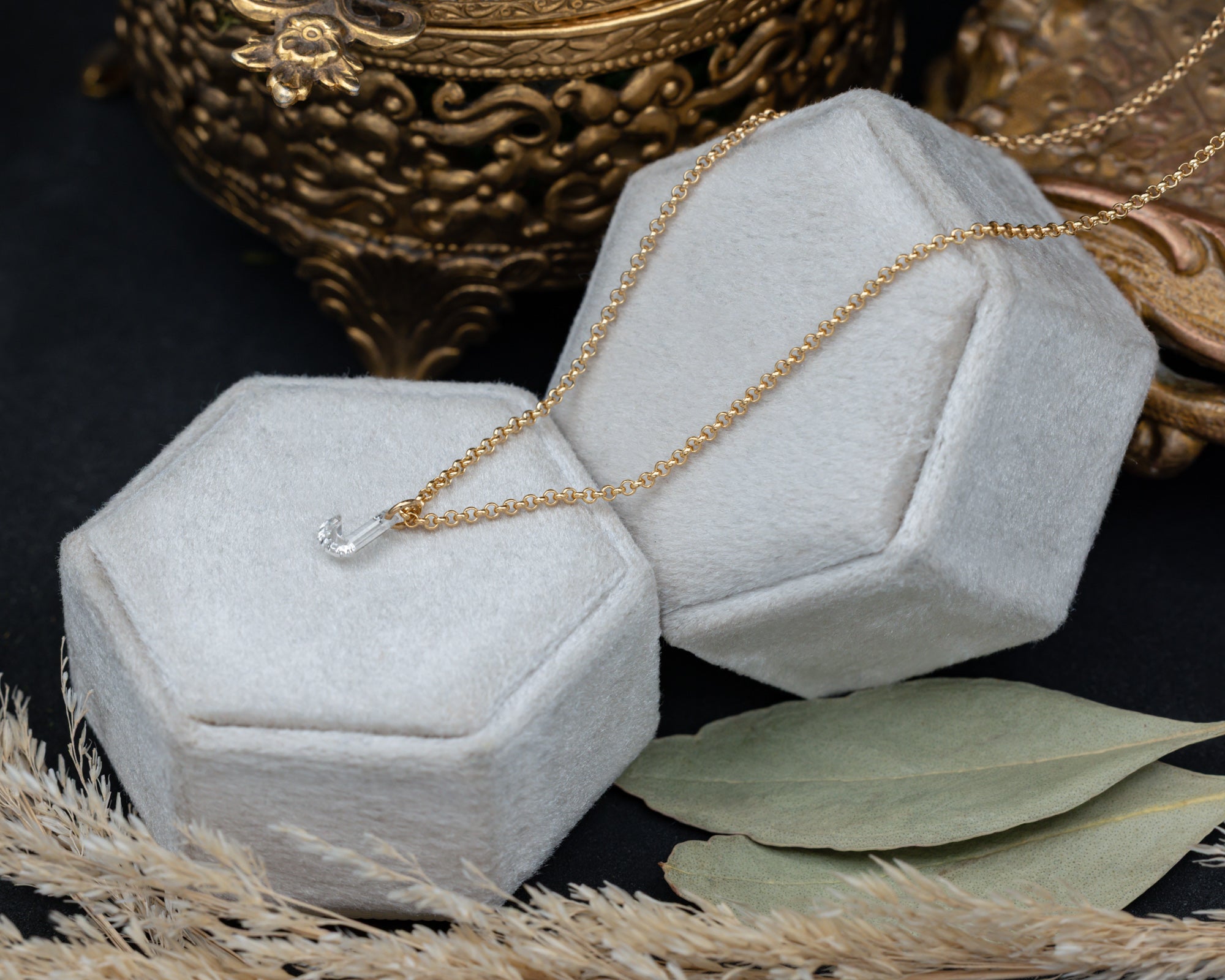 Gold necklace on a hexagonal gray velvet jewelry box with decorative elements in the background.