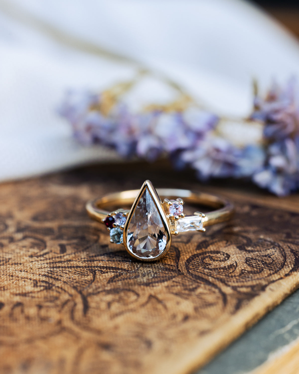 Gold ring with a pear-cut gemstone on a textured surface with a floral background