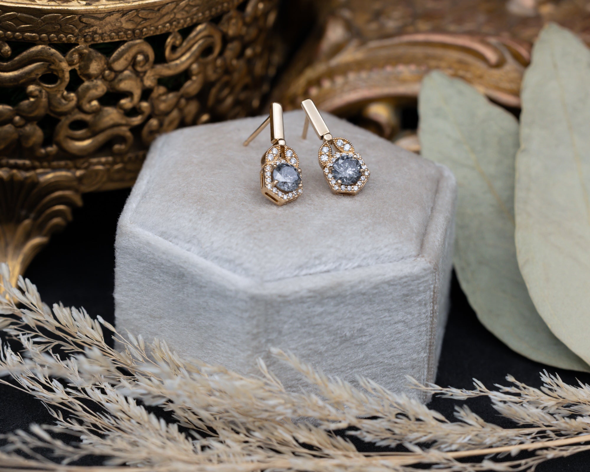 Gold earrings with salt and pepper diamond centerstones in a hexagonal jewelry box.