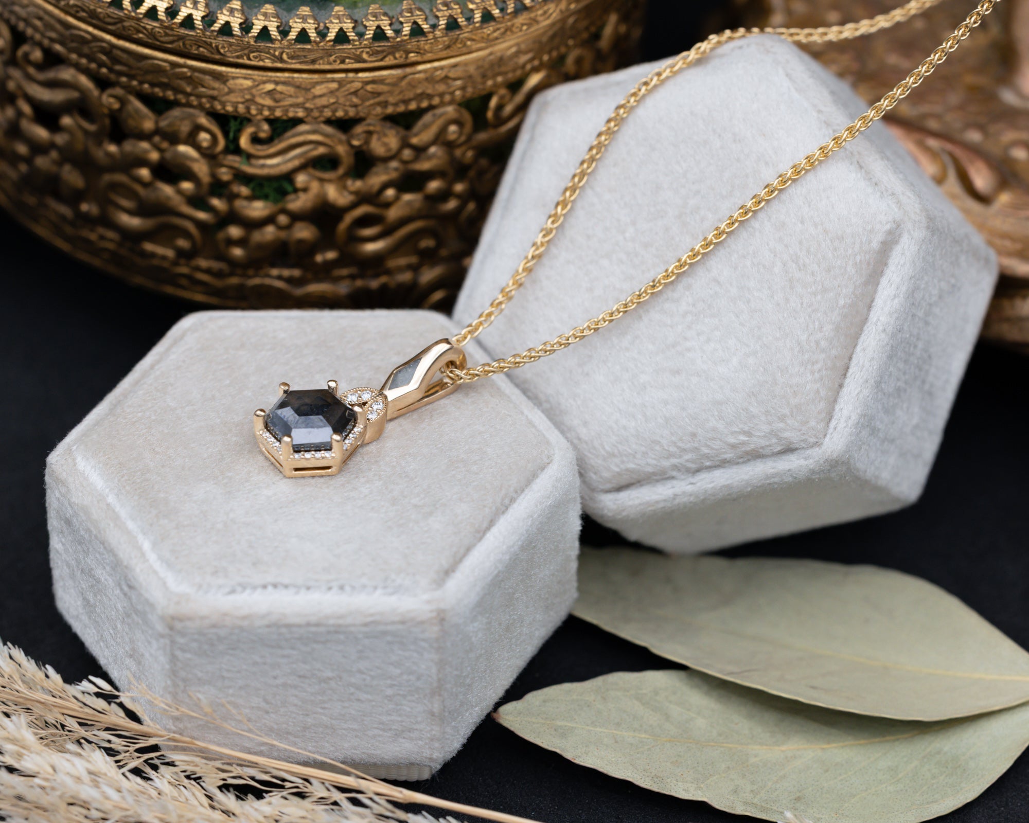 Gold necklace with a salt & pepper diamond pendant on a hexagonal gray velvet stand.