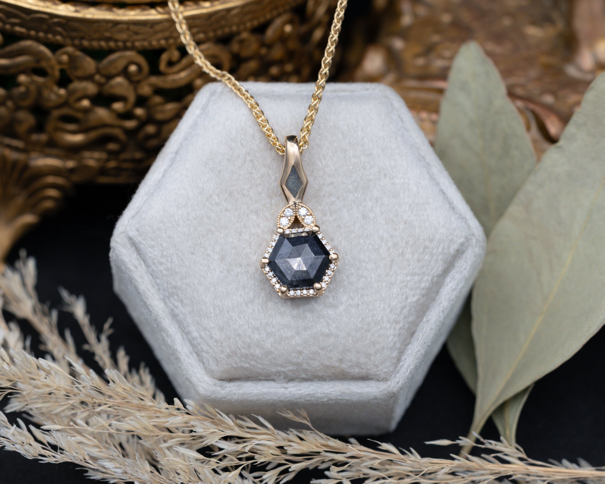 Gold necklace with a salt & pepper diamond pendant on a hexagonal gray velvet stand.