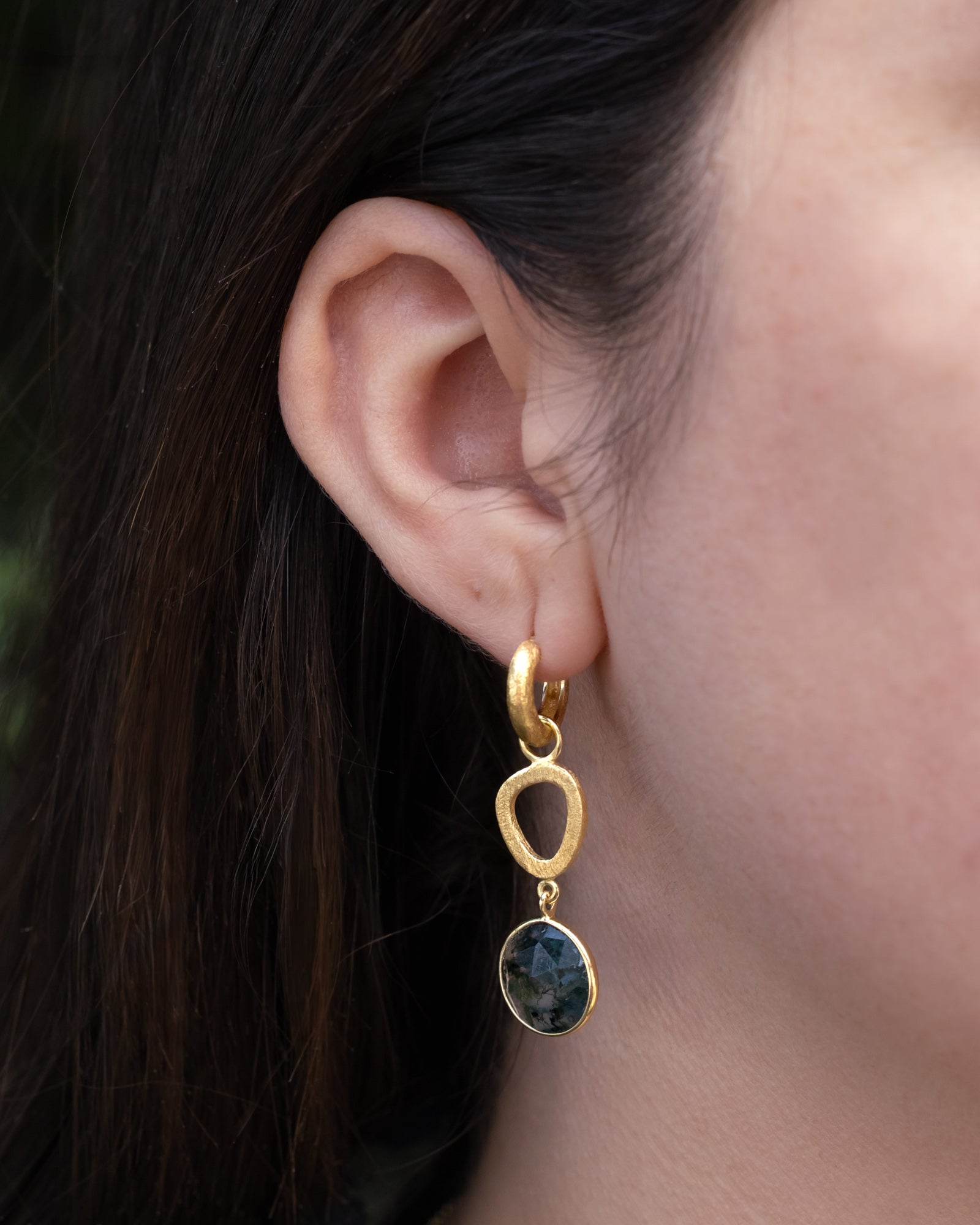 Gold earring with a moss agate gemstone worn by a person