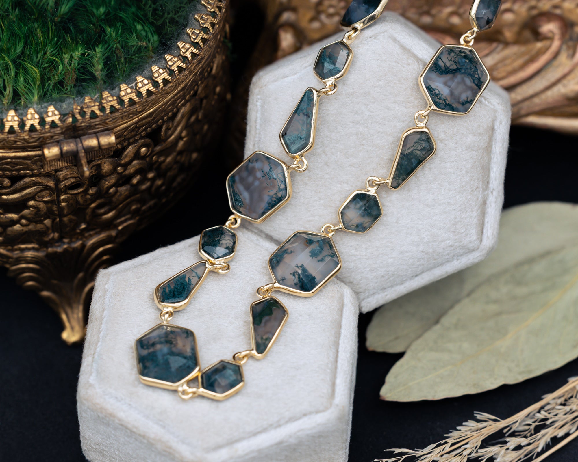 Necklace with moss agate pendants on a white stand with a decorative background