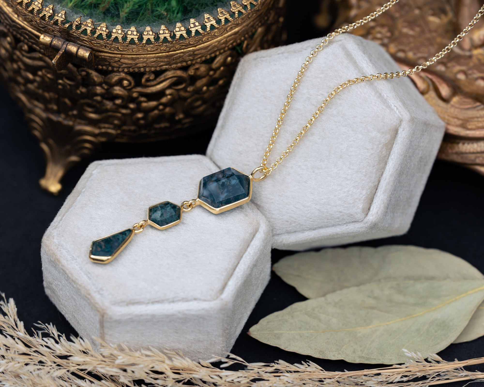 Necklace with moss agate and gold chain on a hexagon cushion with decorative elements in the background