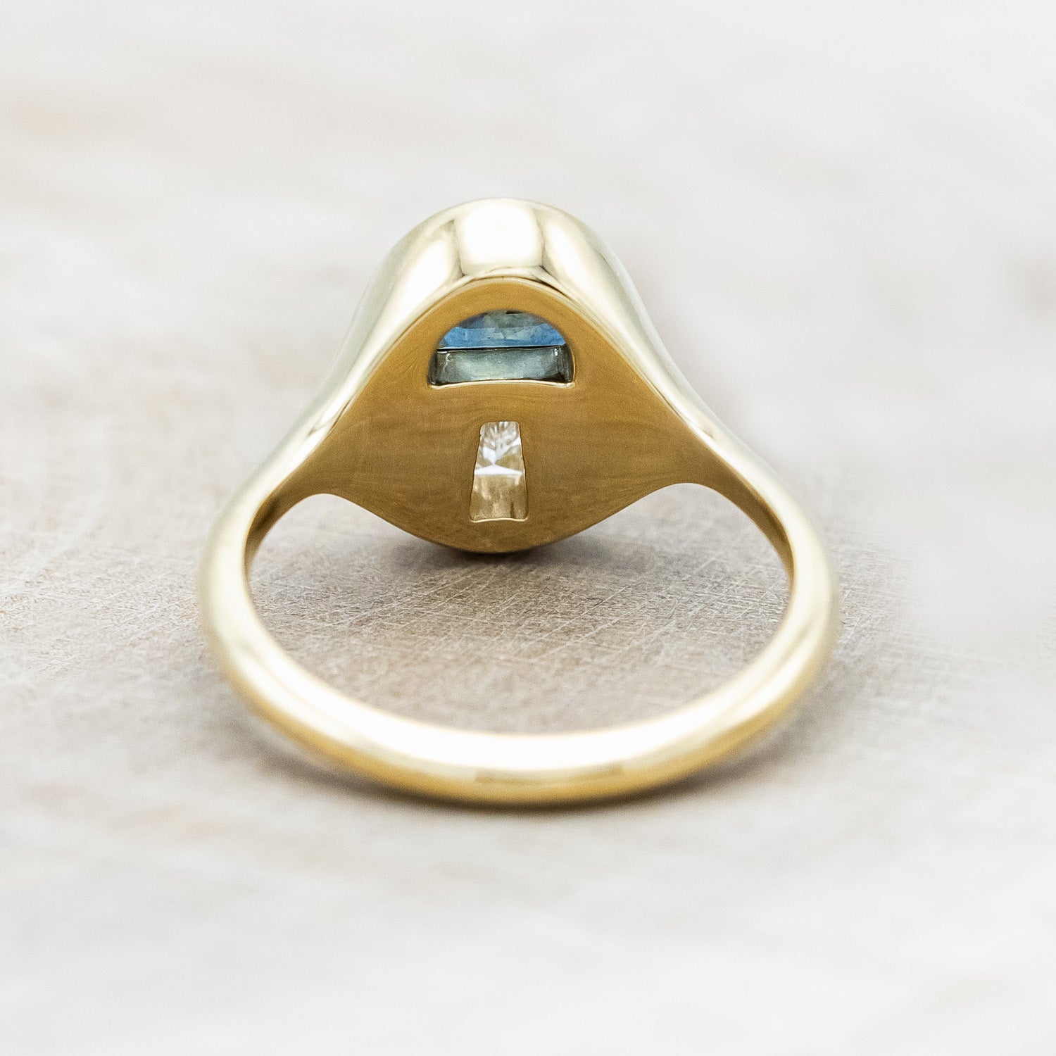 Back of a 14K yellow gold signet ring with a half moon gem cap, tapered baguette diamond stem, and vines engraved on both sides.
