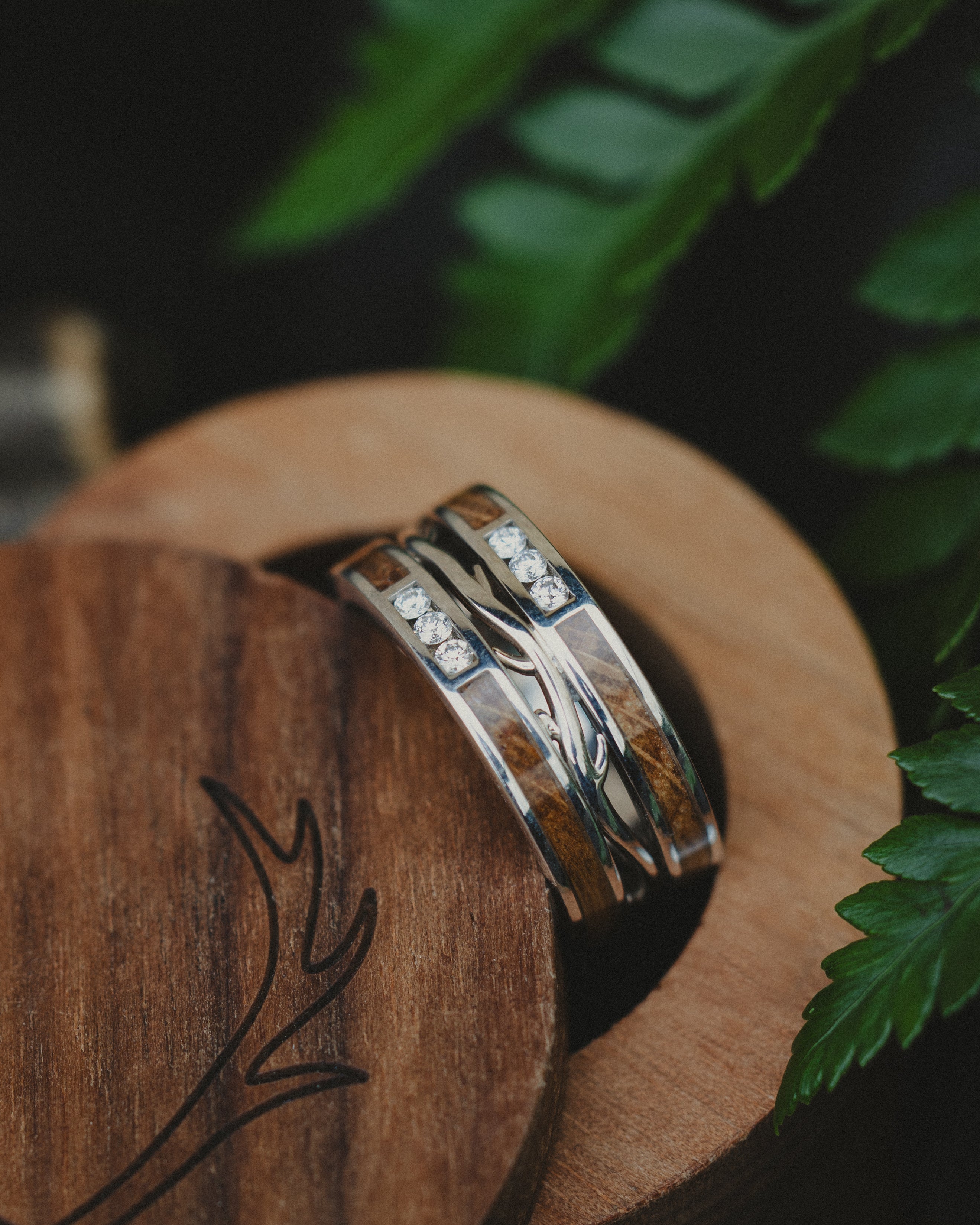 Silver wedding band with wood inlay and diamond accents in a wooden ring box against a natural background