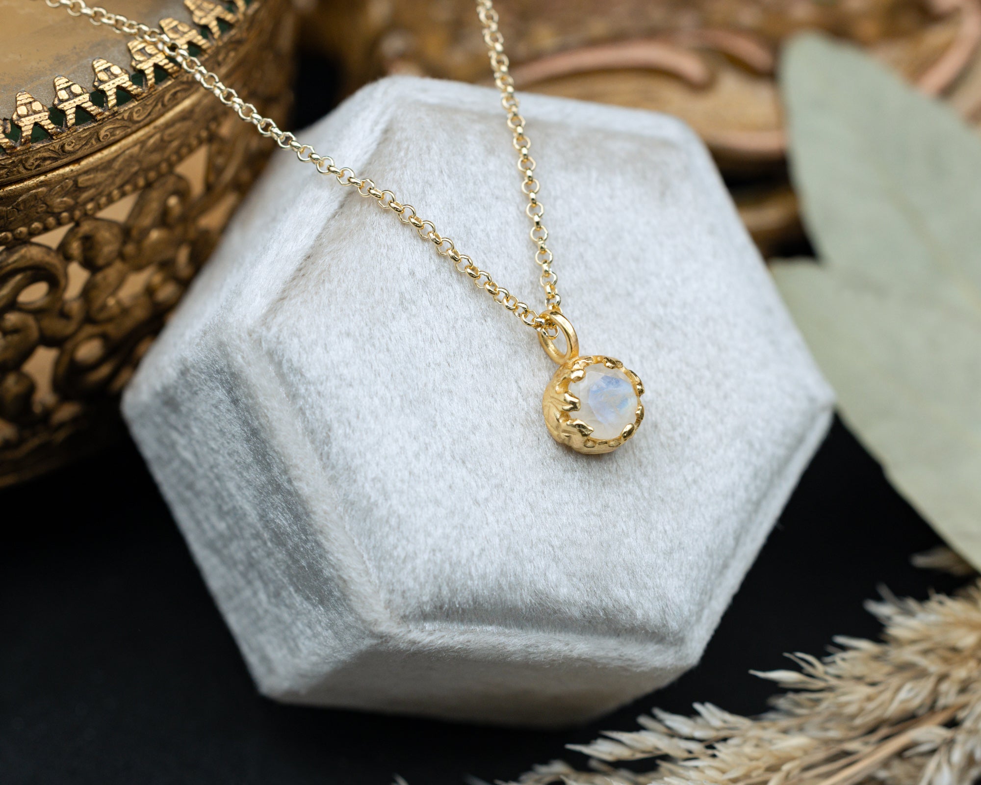 Gold moonstone necklace with a pendant on a white hexagonal cushion