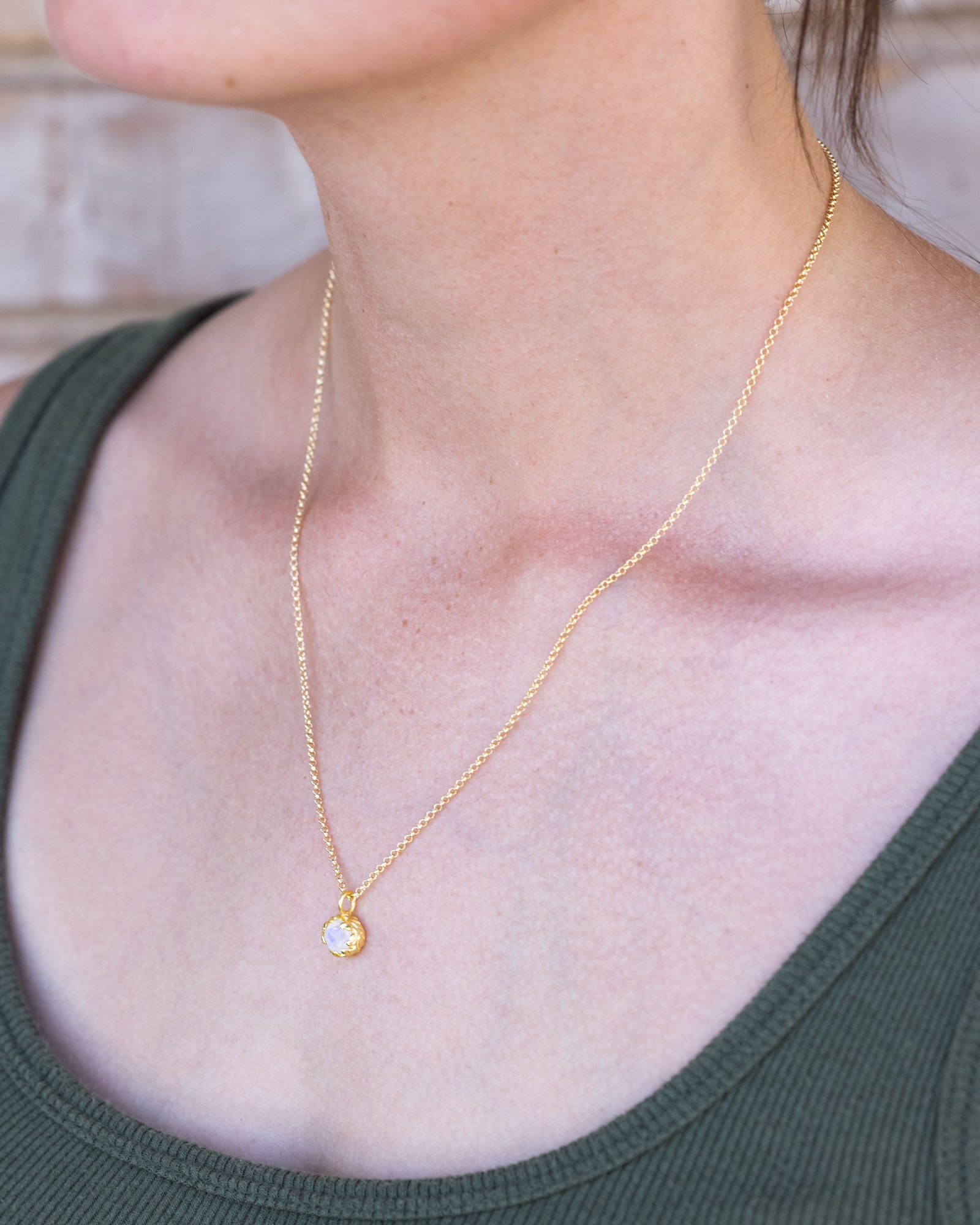 Gold necklace with a moonstone pendant on a person wearing a green top.