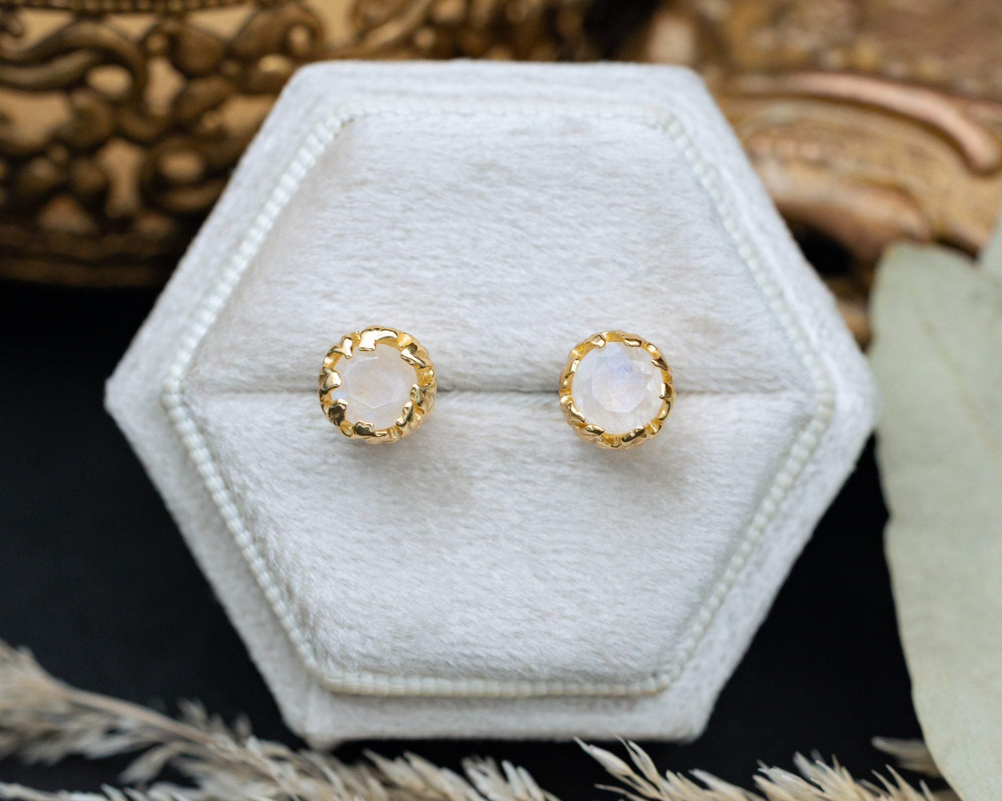 Gold earrings with moonstone on a hexagonal white stand.