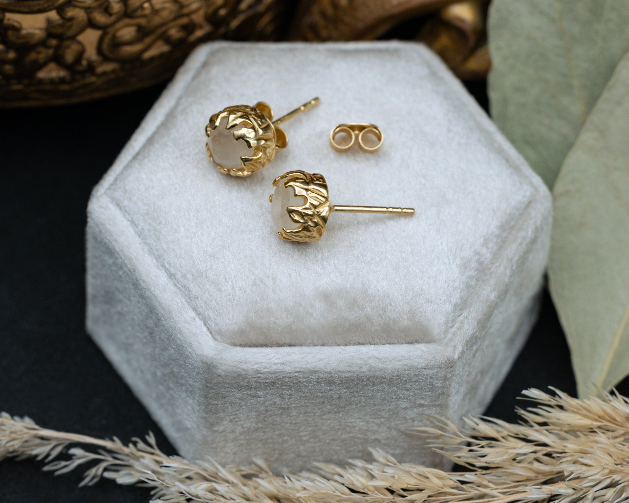 Gold moonstone earrings on a white hexagonal jewelry box with a decorative background