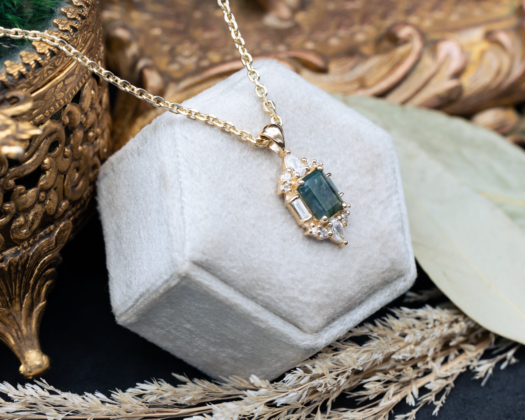Gold necklace with a moss agate pendant on a hexagonal gray velvet stand.