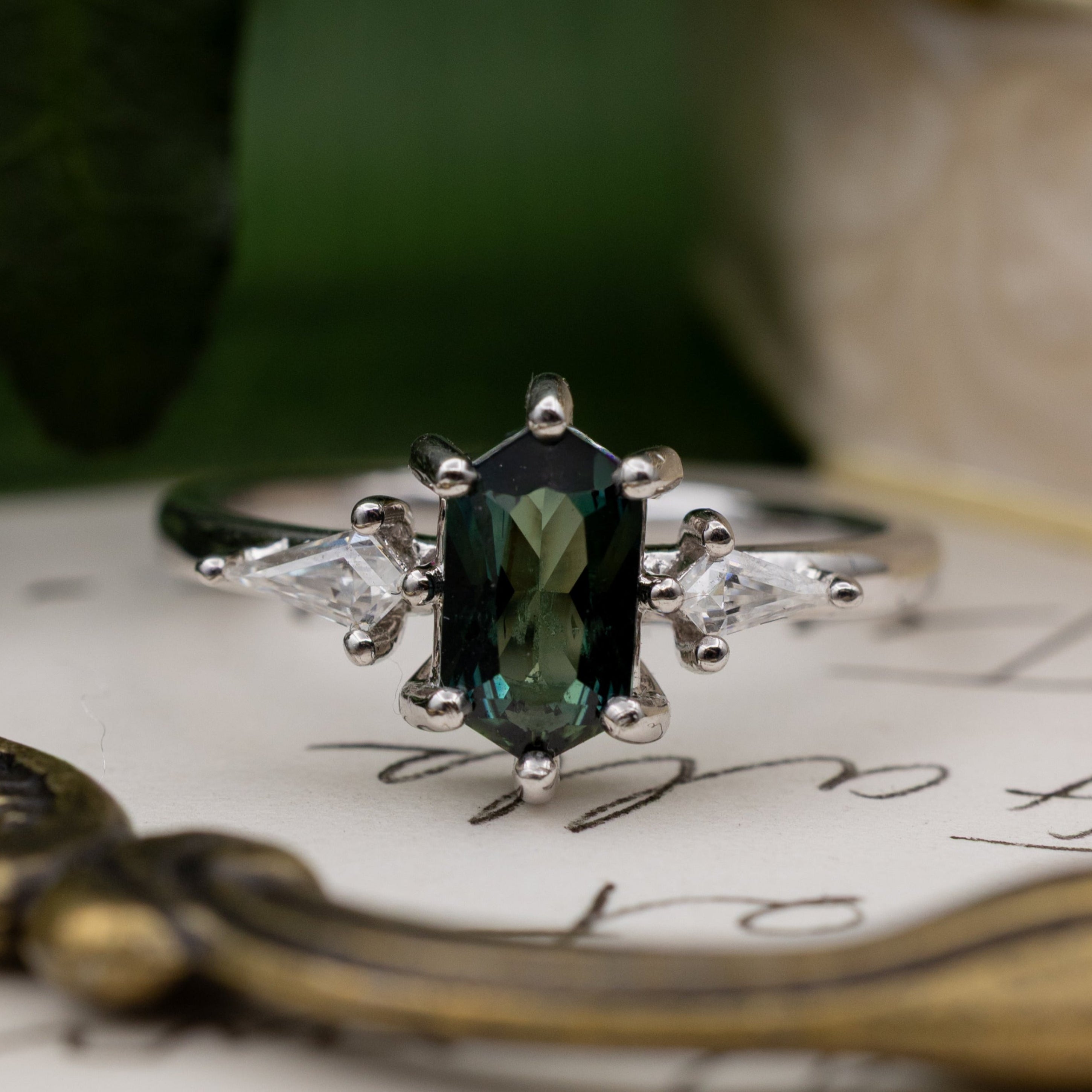 White gold ring with a green sapphire on an old letter with decorative elements.