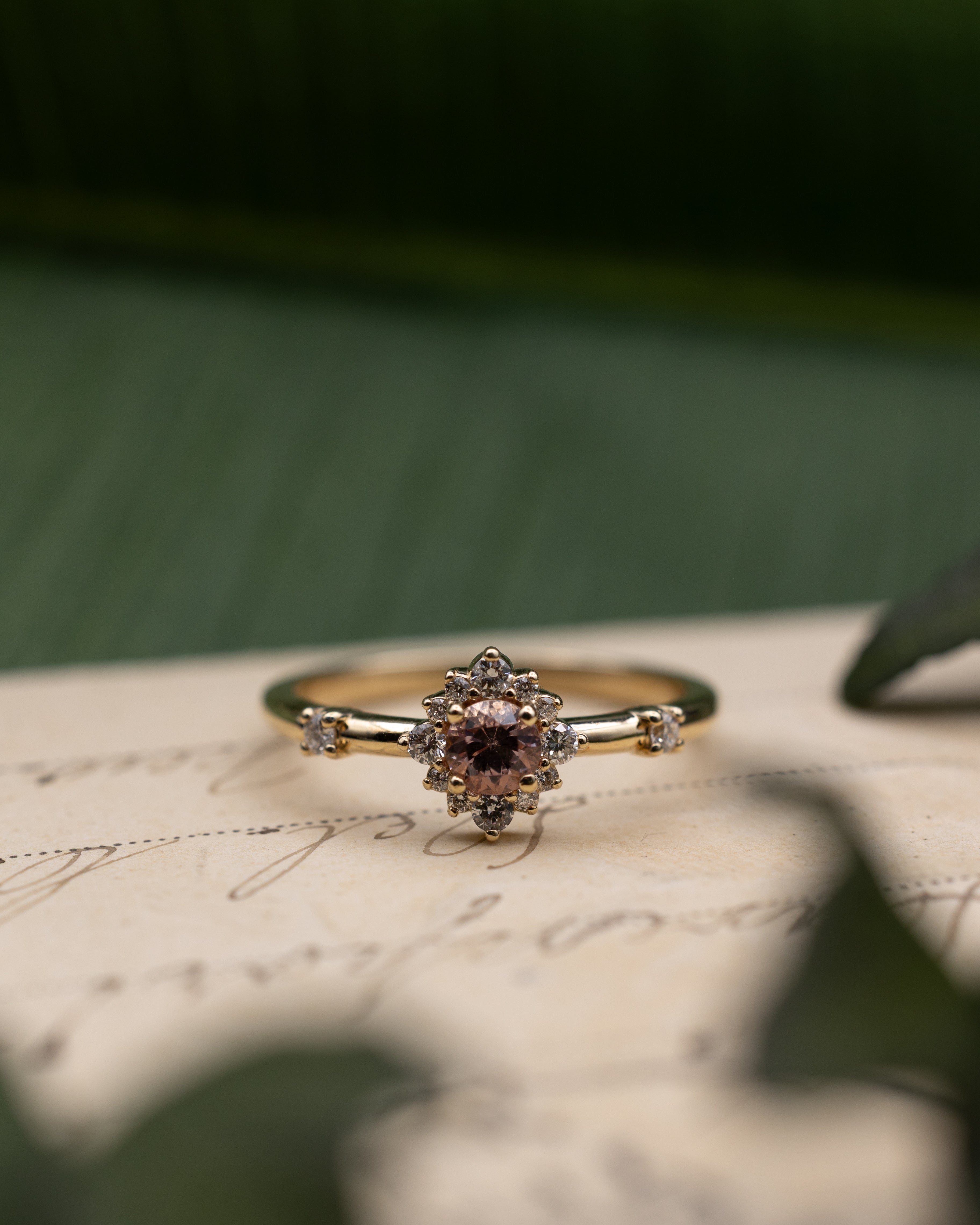 Yellow gold ring with dragon garnet center stone and diamond accents on a vintage letter against a blurred green background