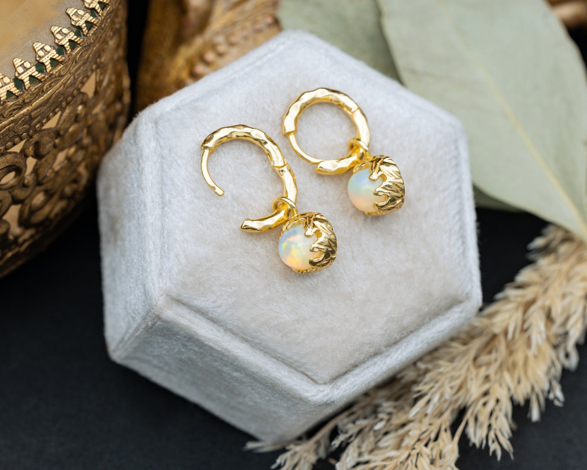 Gold hoop earrings with opal stones on a hexagonal white pillow.