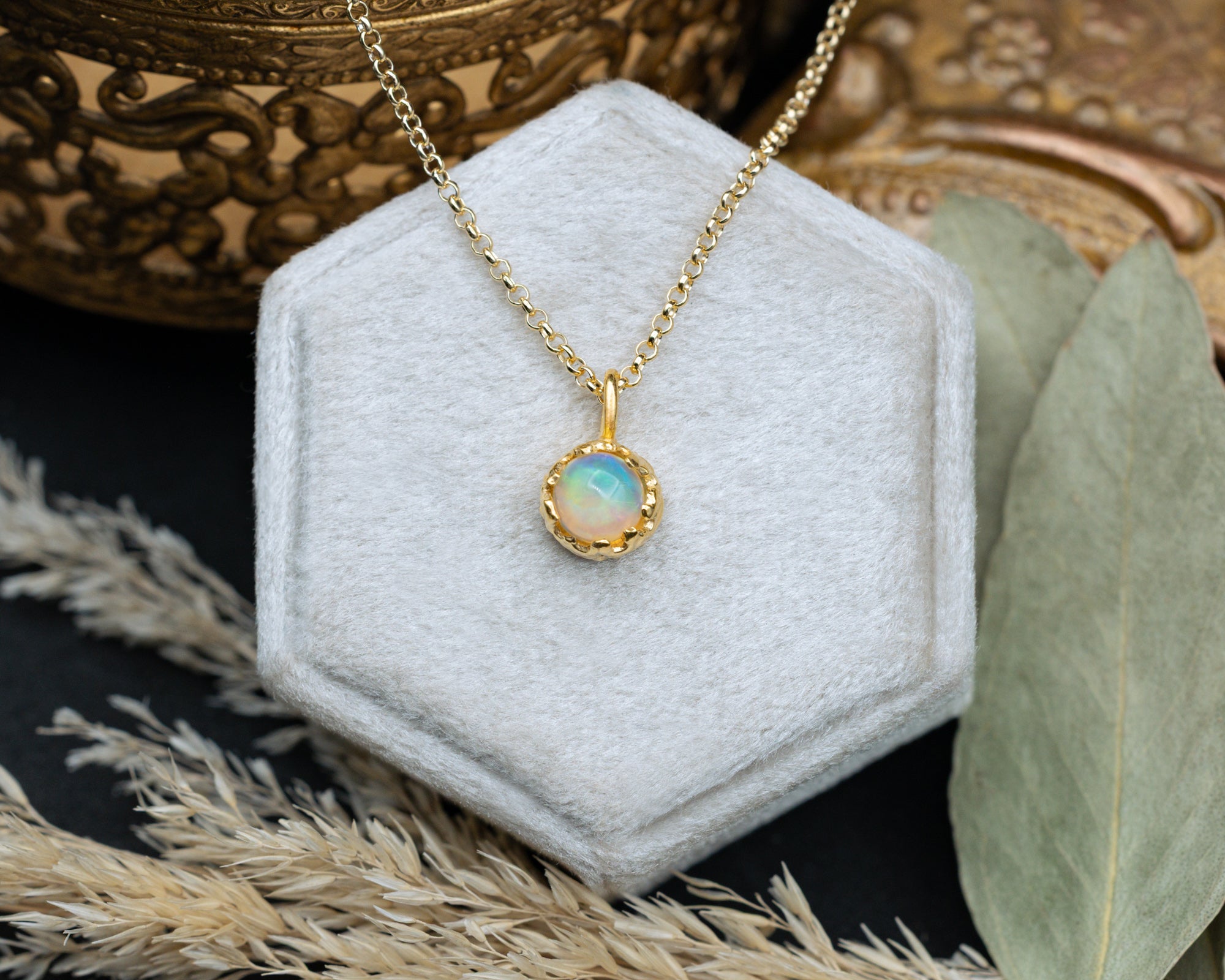 Gold necklace with an opal pendant on a white cushion, surrounded by decorative elements.