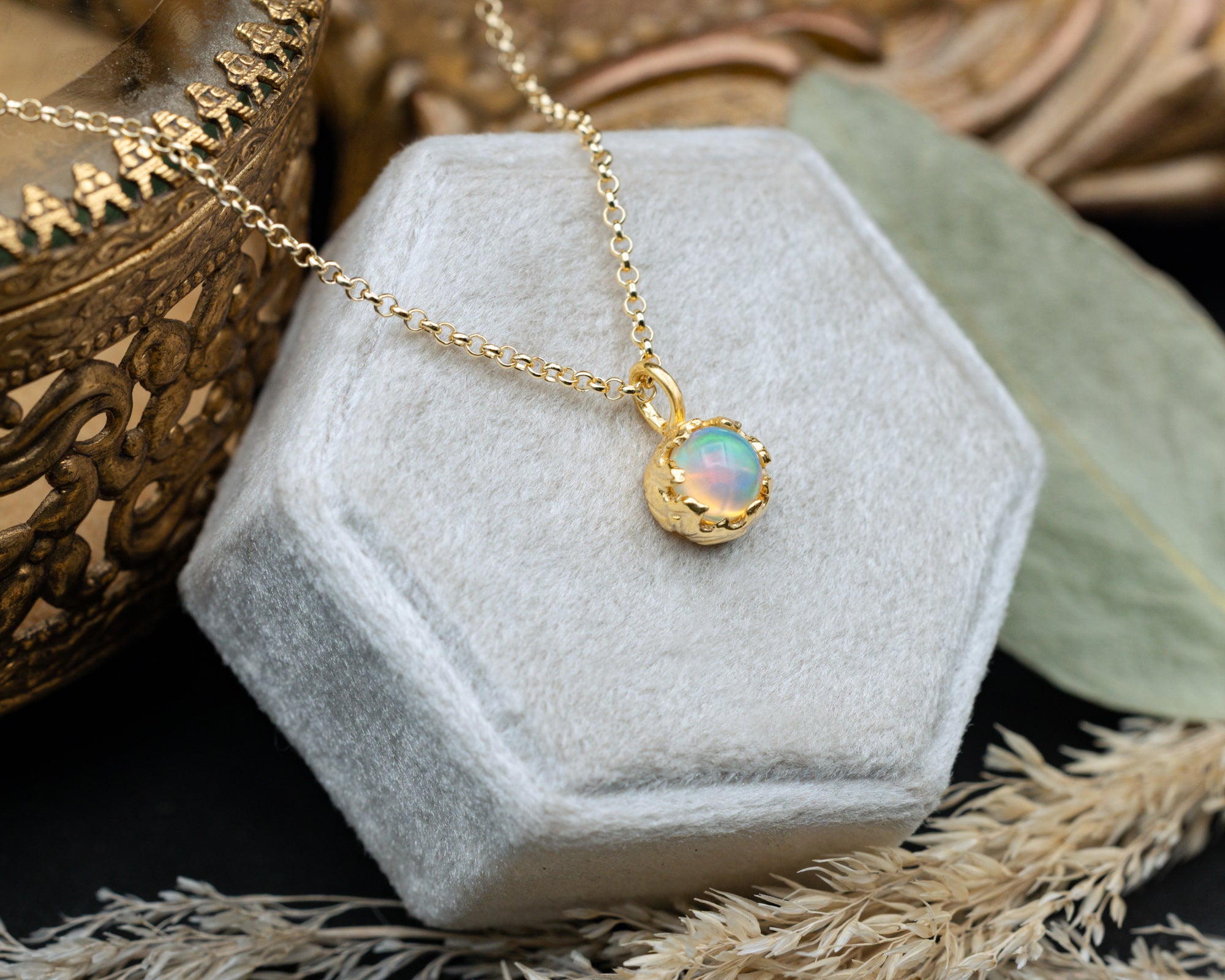 Gold necklace with an opal pendant on a hexagonal gray cushion