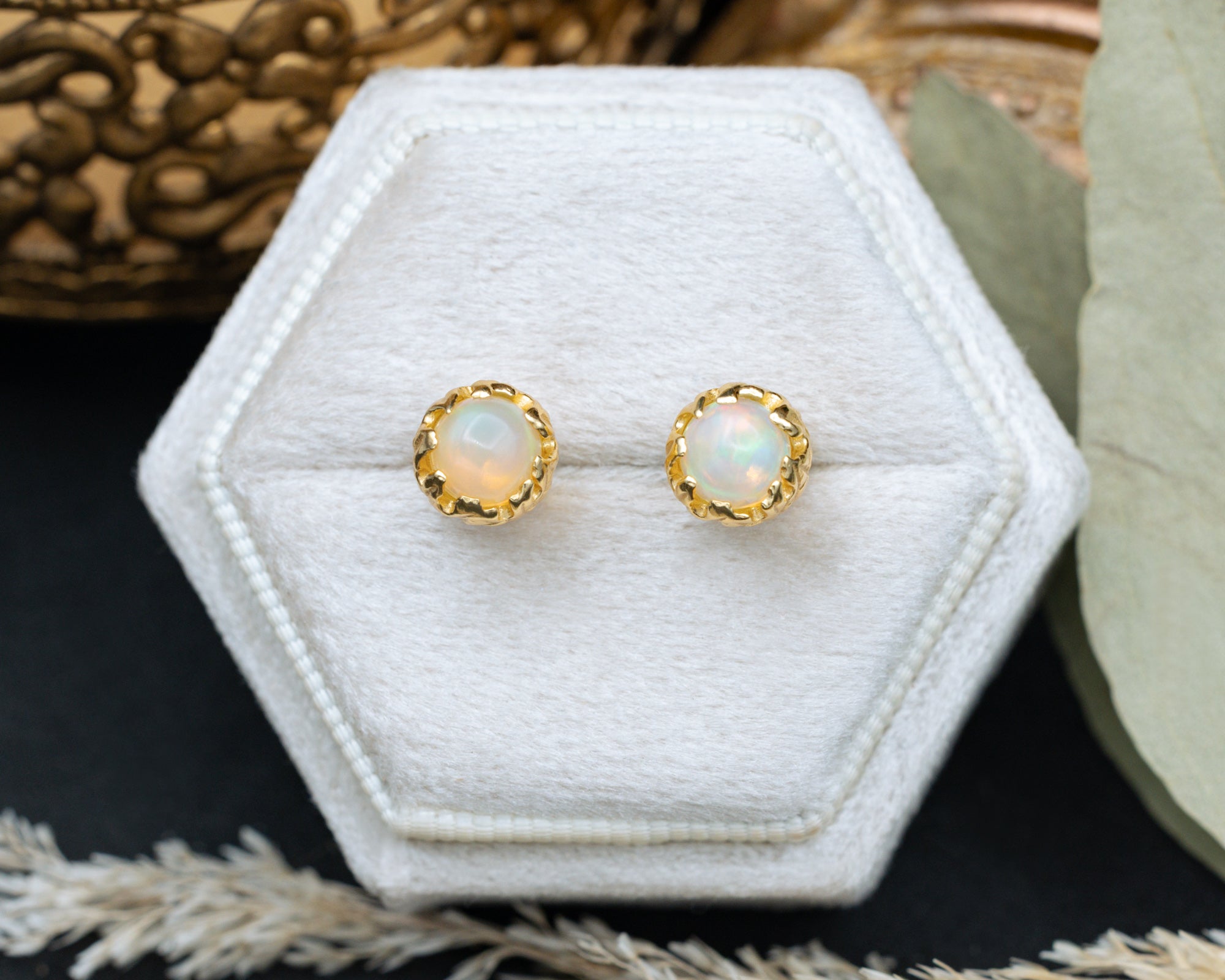 Opal earrings in a gold setting on a hexagonal white jewelry display.