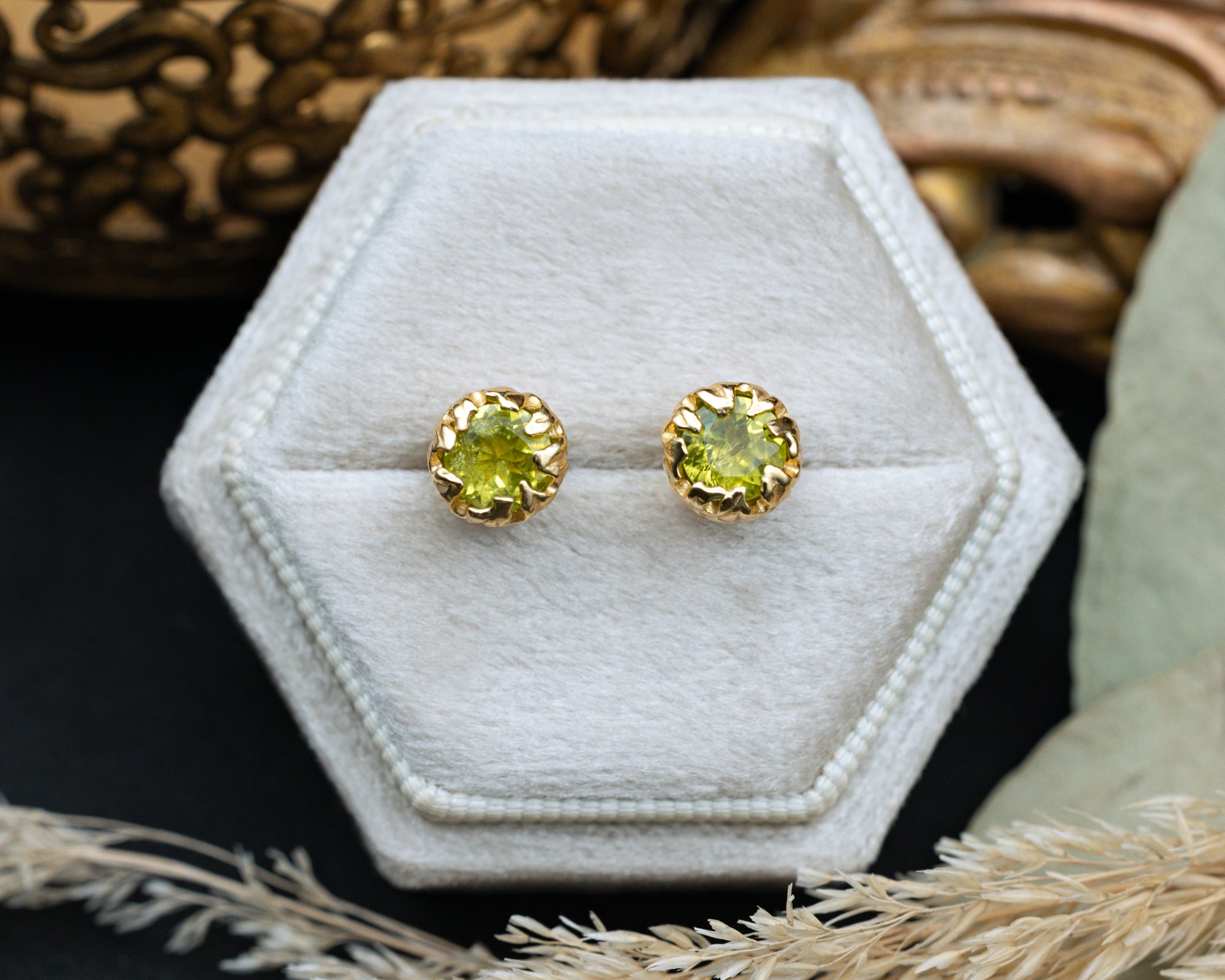 Gold earrings with green peridot on a hexagonal white pillow.