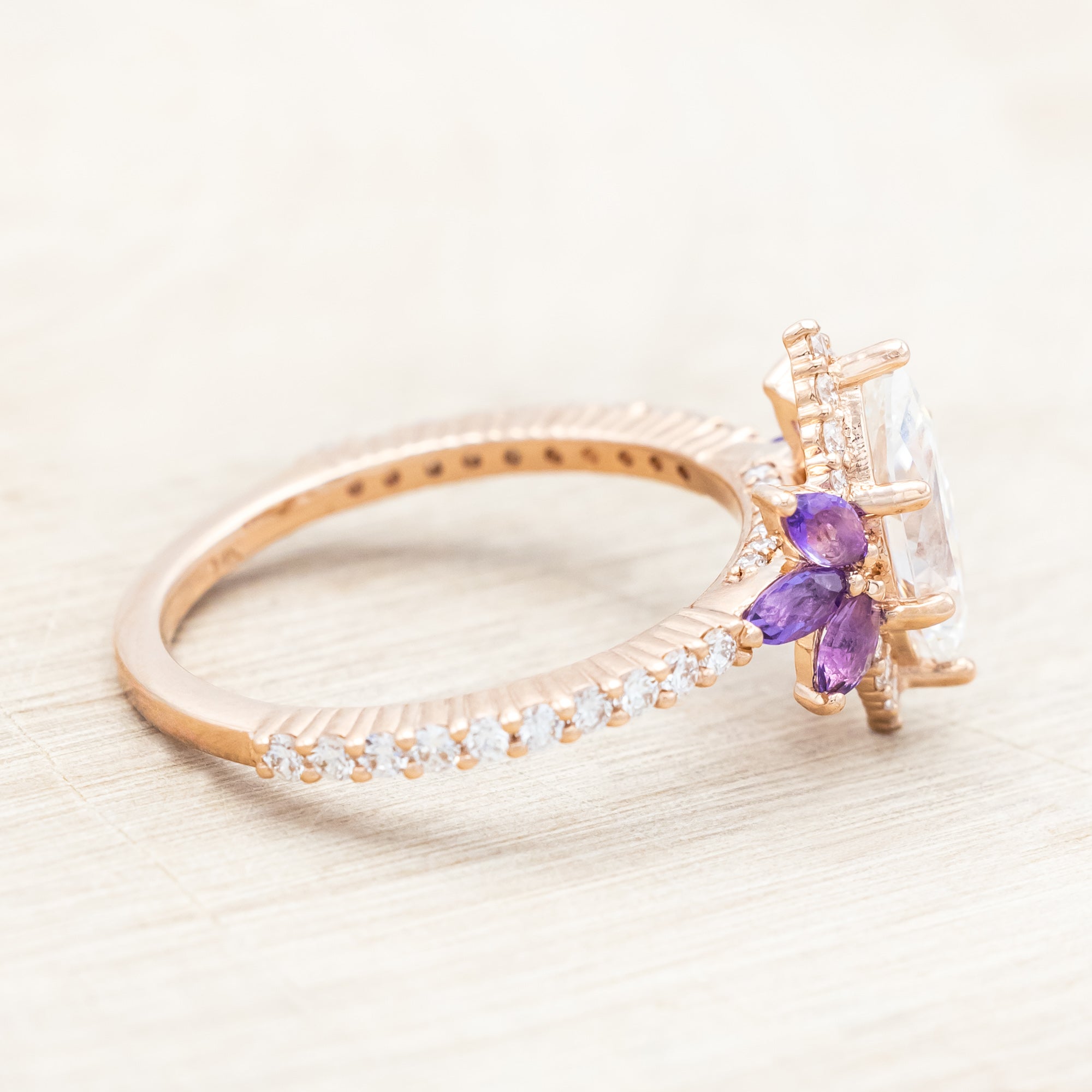 14K Rose gold ring with a moissanite center stone and small purple amethyst accents on a light wooden background