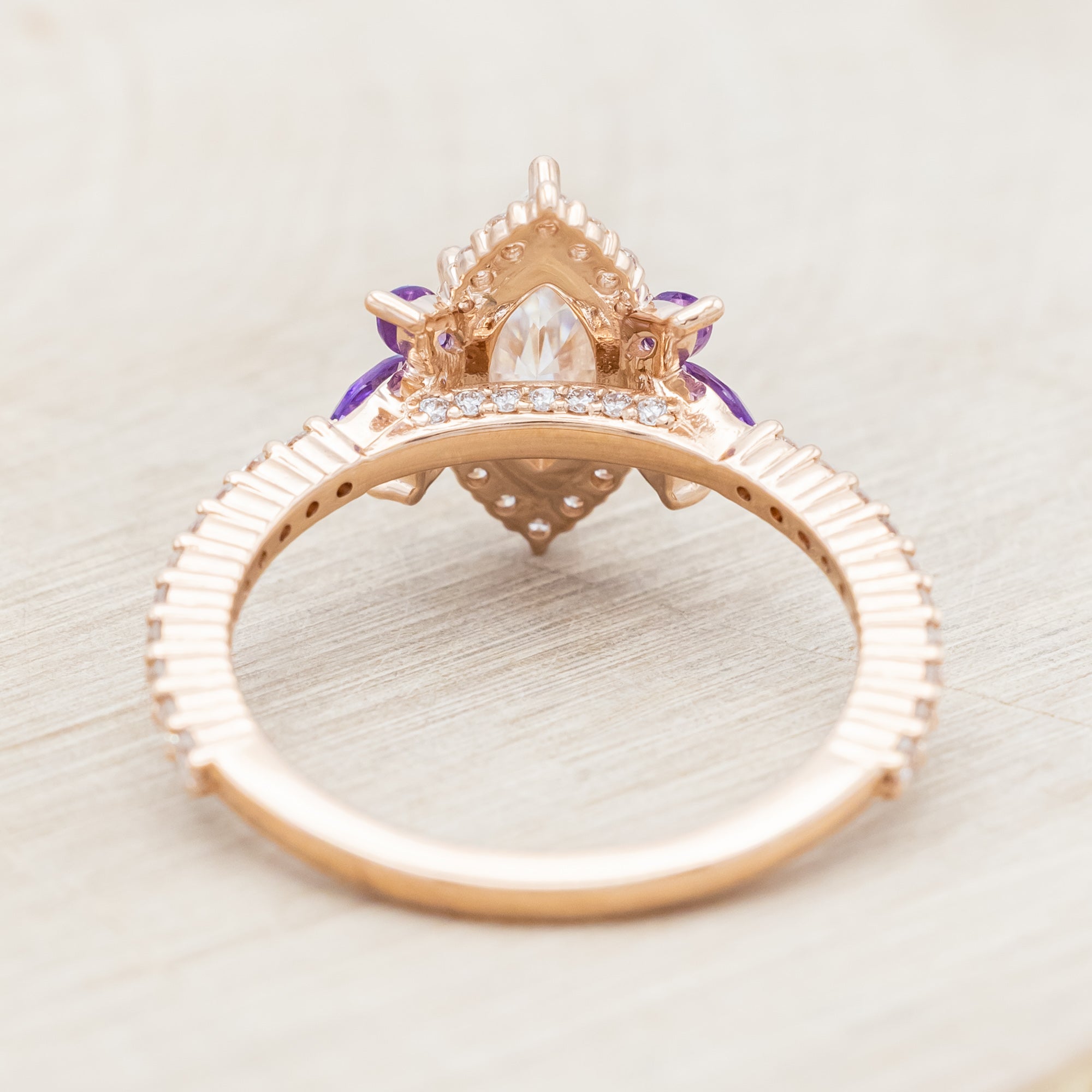 14K Rose gold ring with a moissanite center stone and small purple amethyst accents on a light wooden background