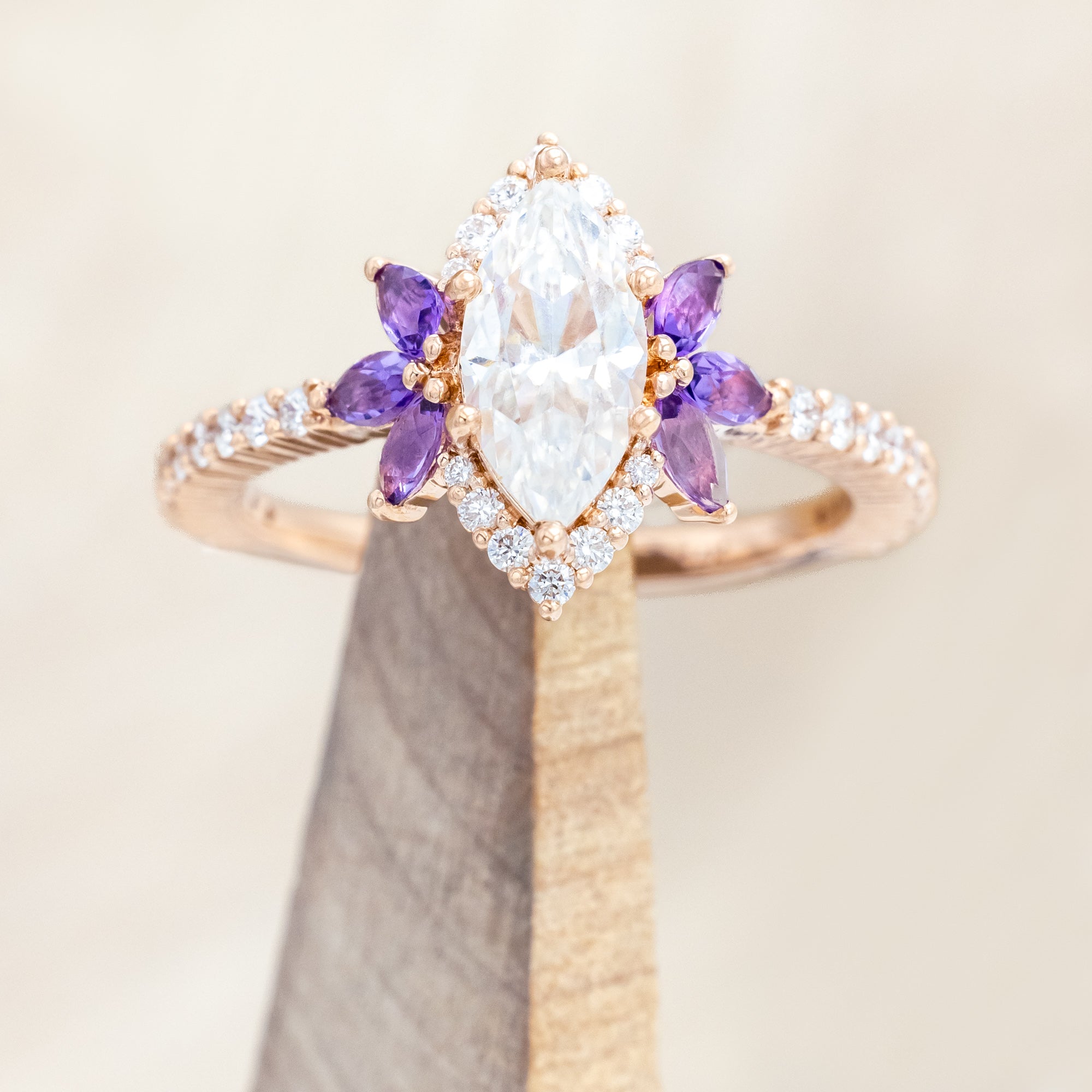 14K Rose gold ring with a moissanite center stone and small purple amethyst accents on a beige background