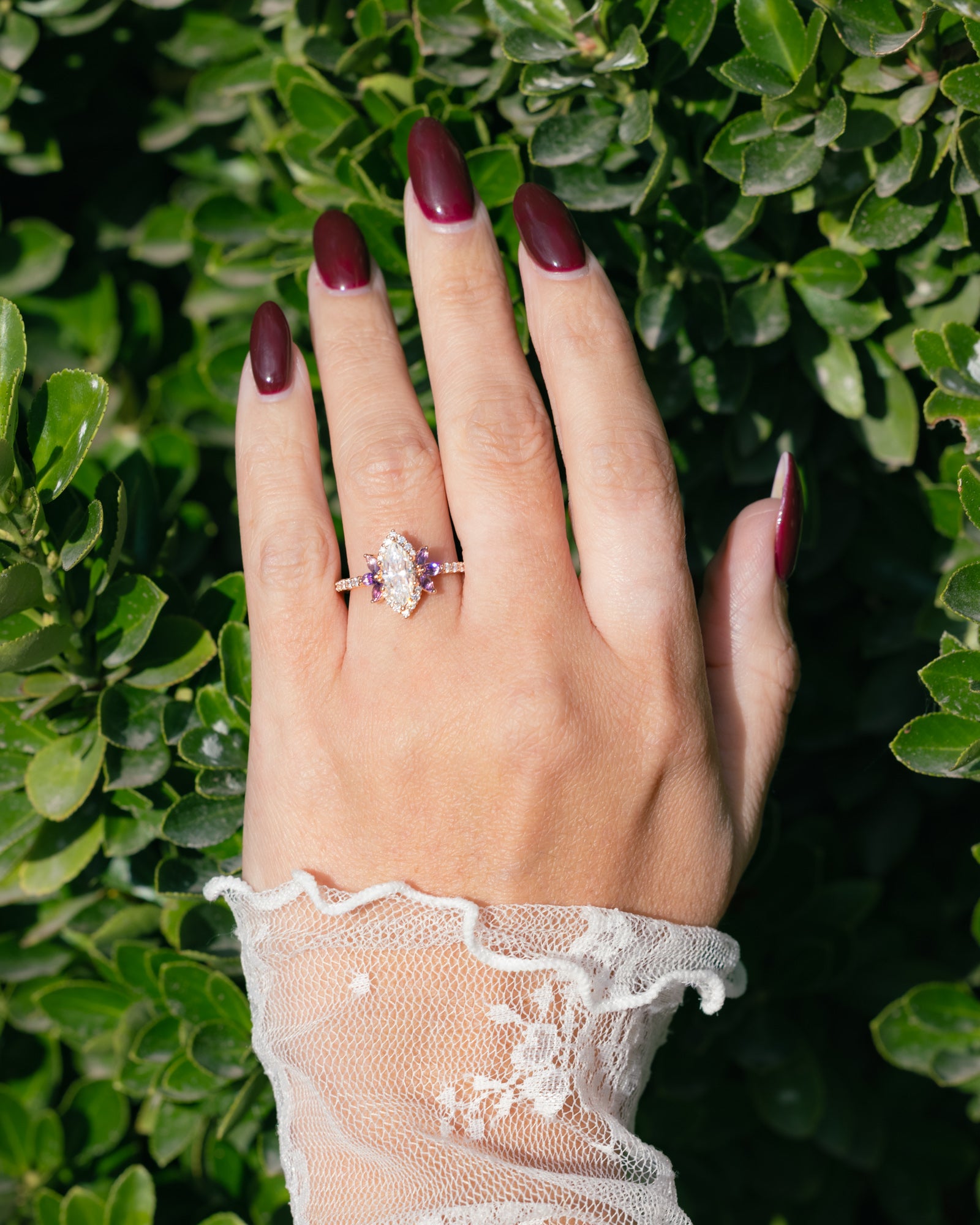 Hand wearing a moissanite and amethyst ring with a green leafy background
