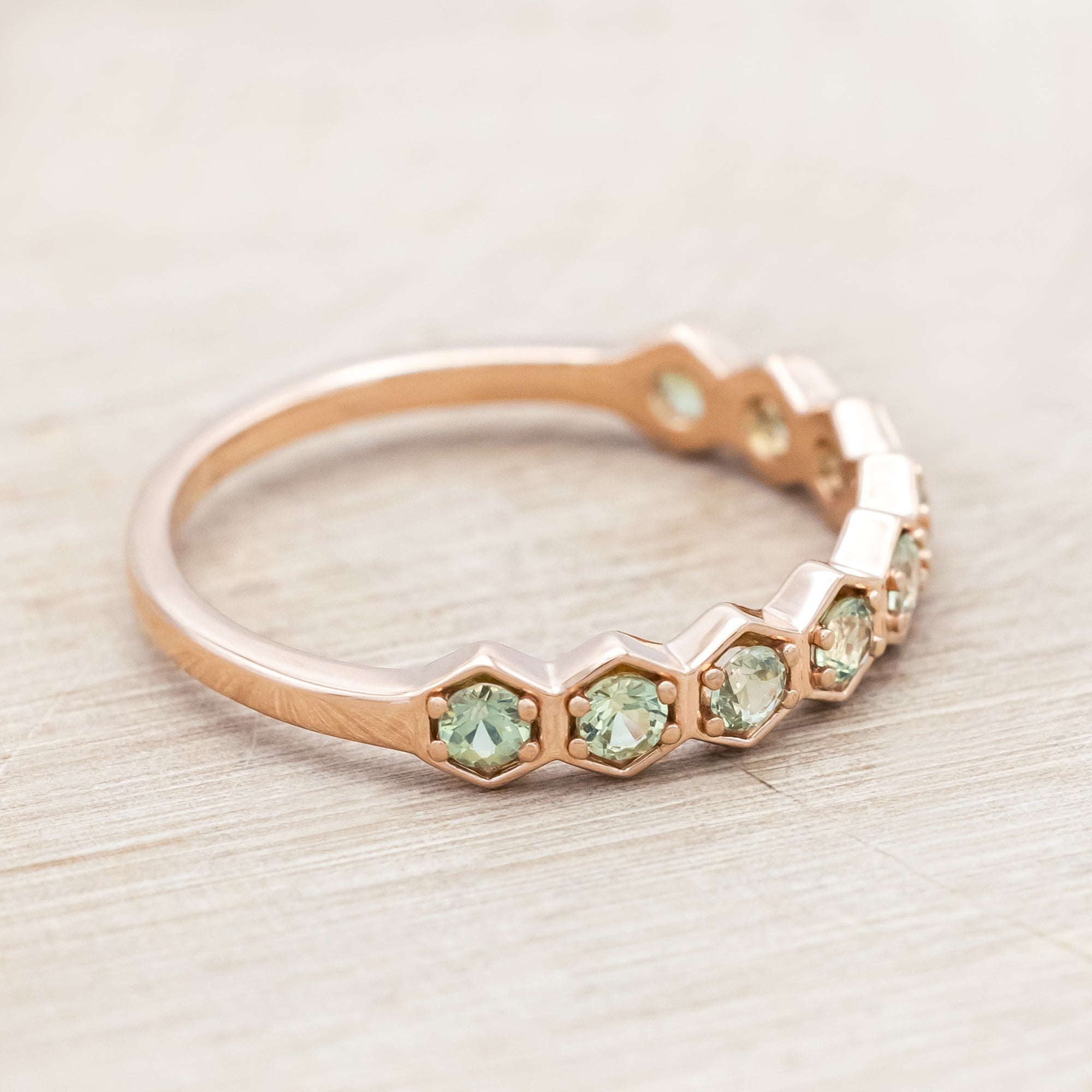 14K rose gold ring with green sapphires on a light wooden surface