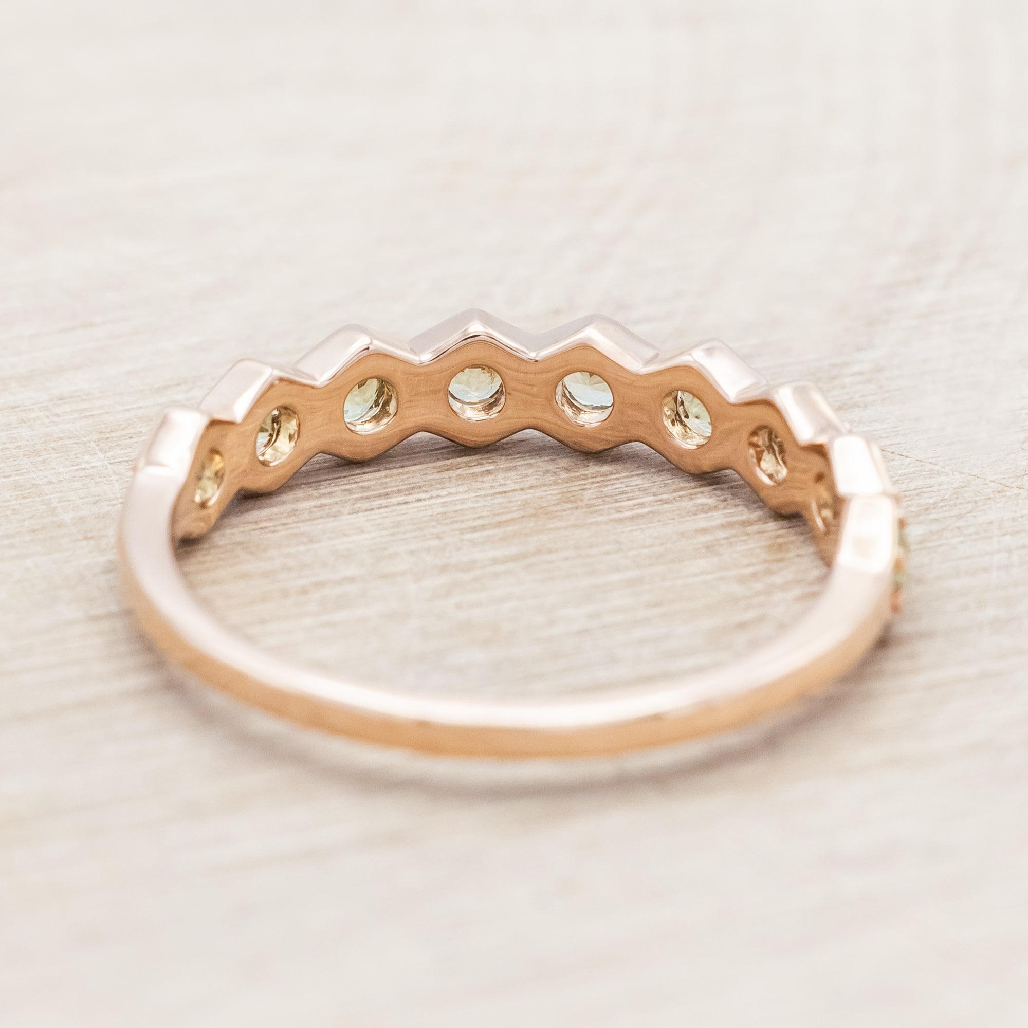 14K rose gold ring with green sapphires on a light wooden surface