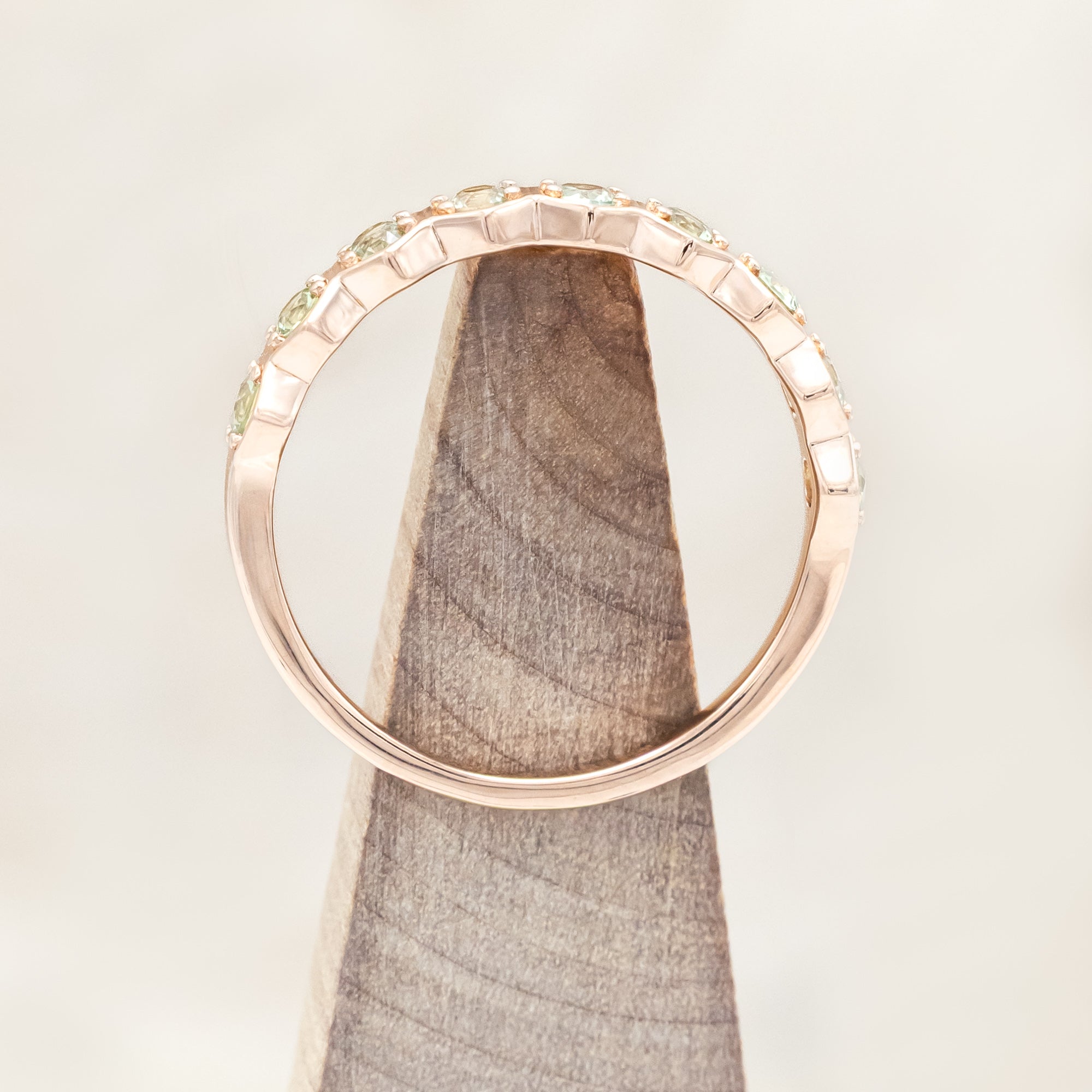 14K rose gold ring with green sapphires on a light background