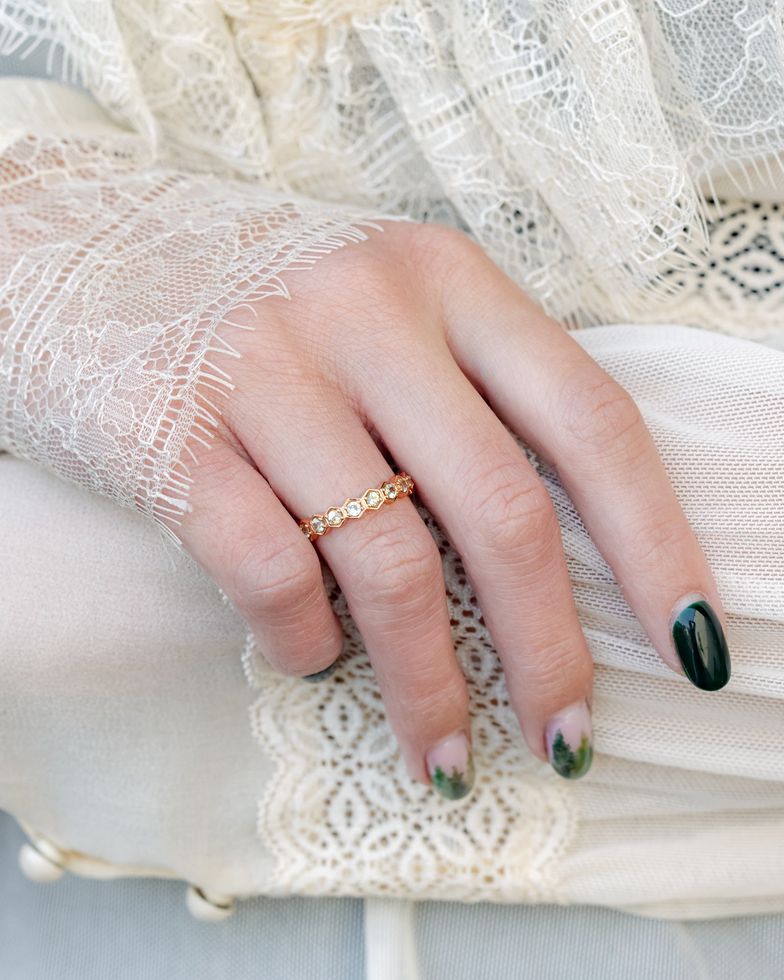 Close-up of a hand wearing a gold ring with a delicate lace background