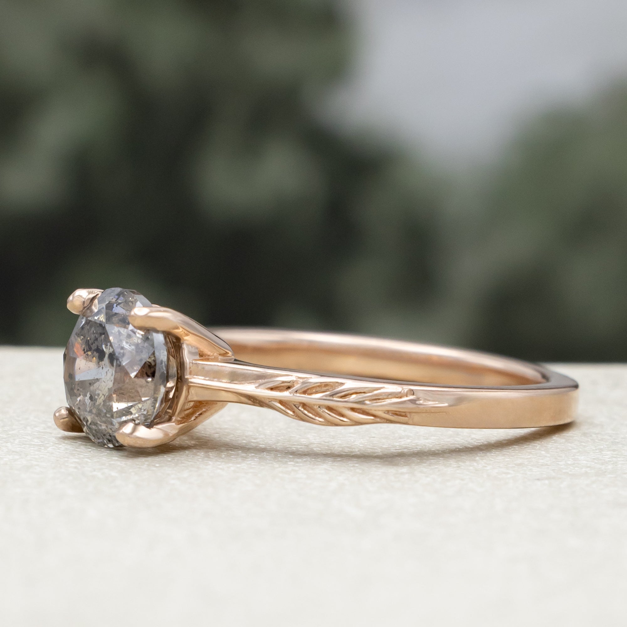 Rose gold ring with round salt & pepper diamond in front of a blurred green background