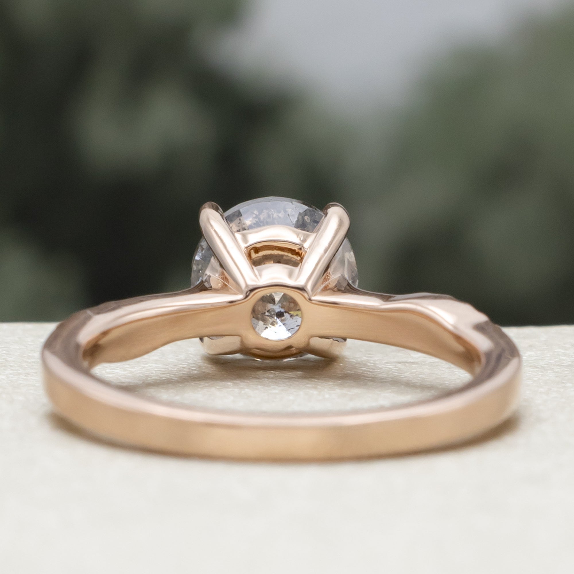 Rose gold ring with round salt & pepper diamond in front of a blurred green background