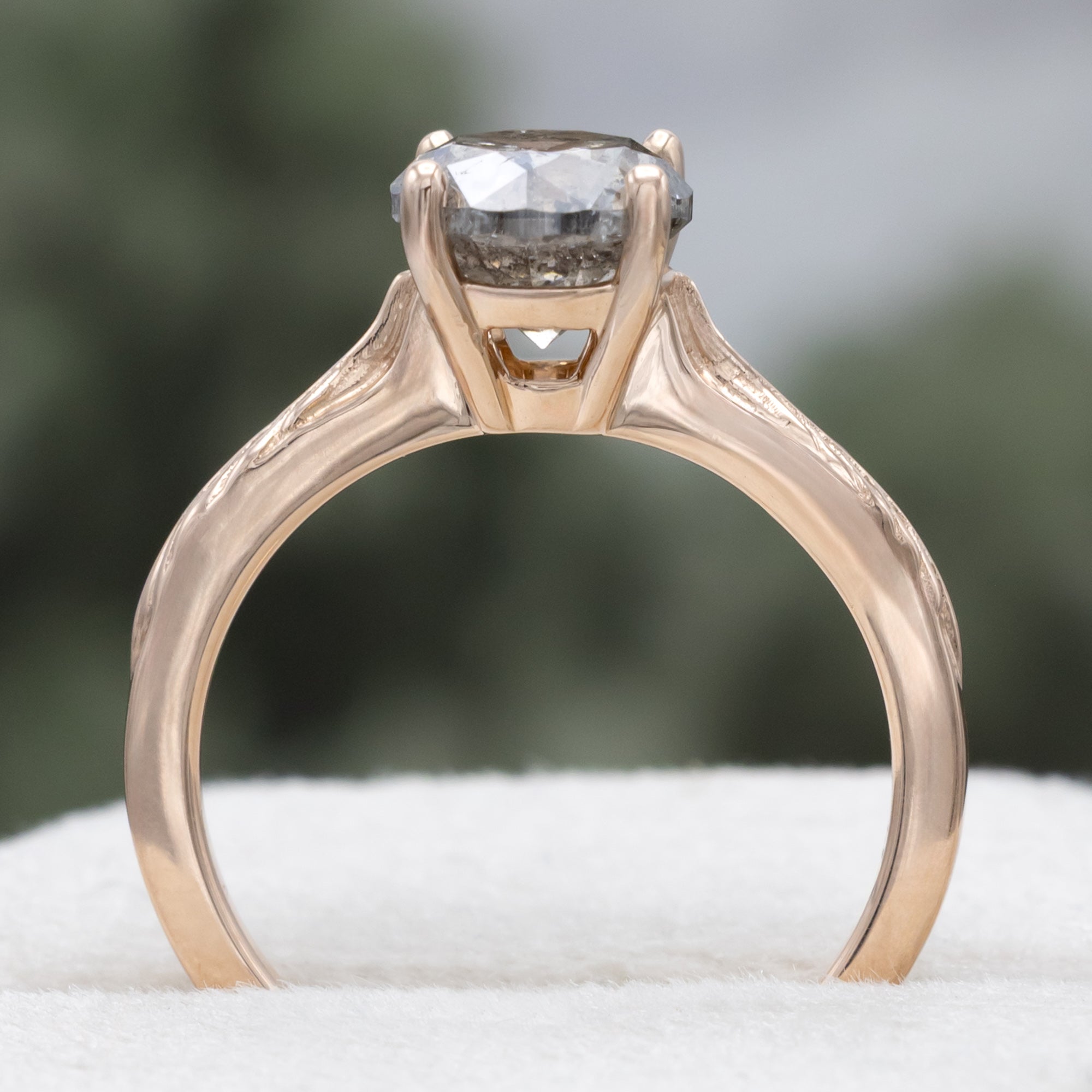 Rose gold ring with round salt & pepper diamond in front of a blurred green background