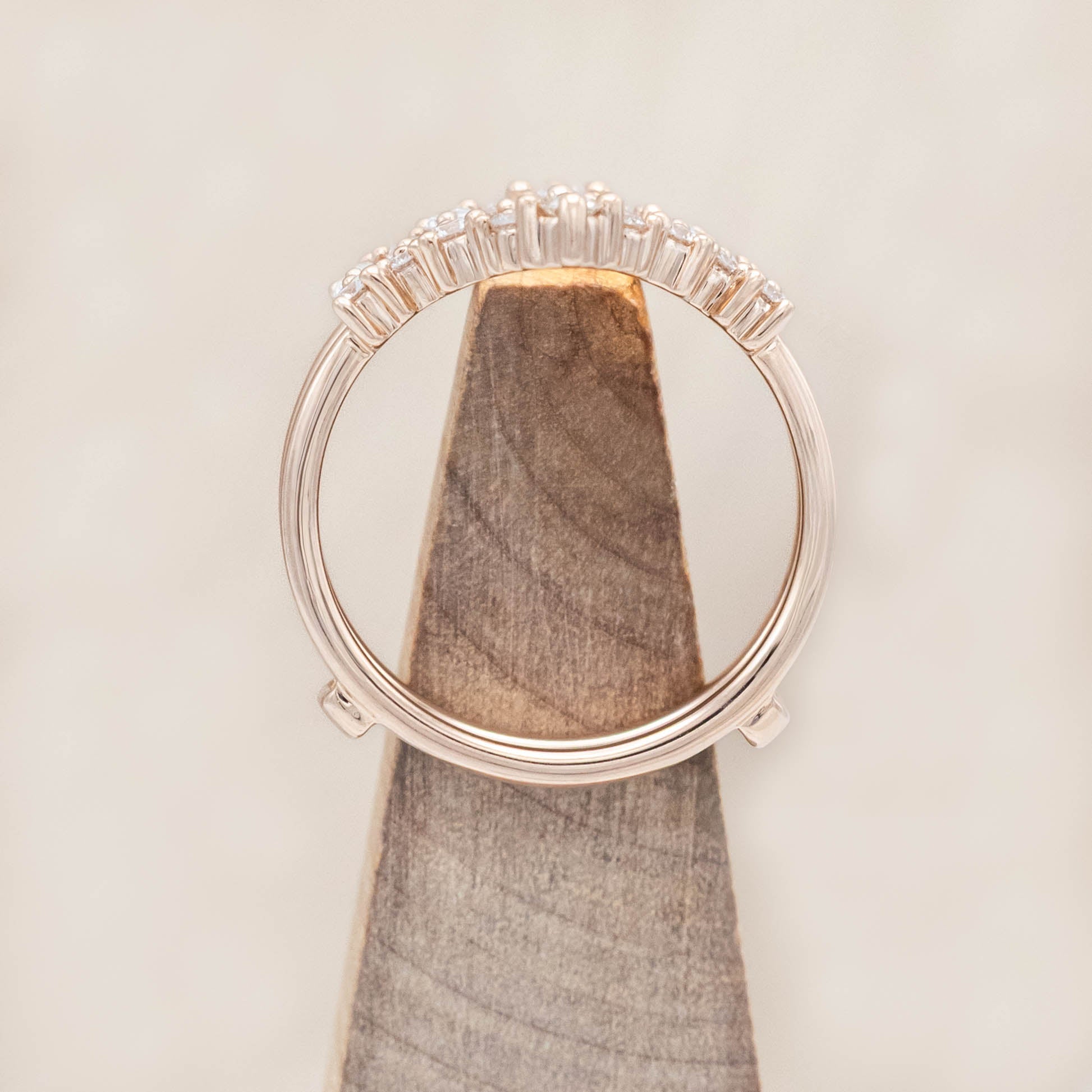 14K rose gold ring with diamond accents on a wooden stand against a beige background
