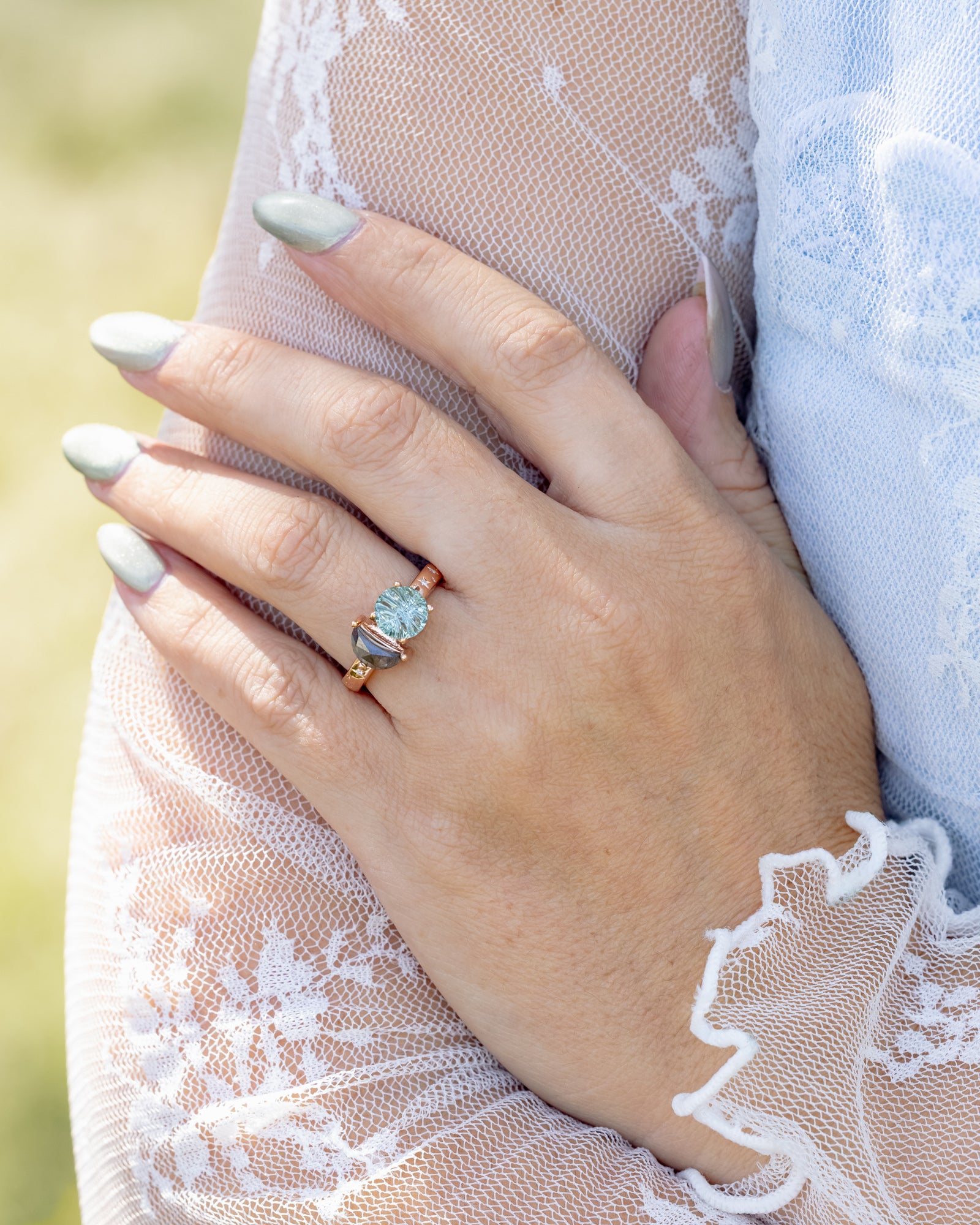 Hand wearing a ring with a sapphire and salt & pepper diamond on a lace-sleeved hand