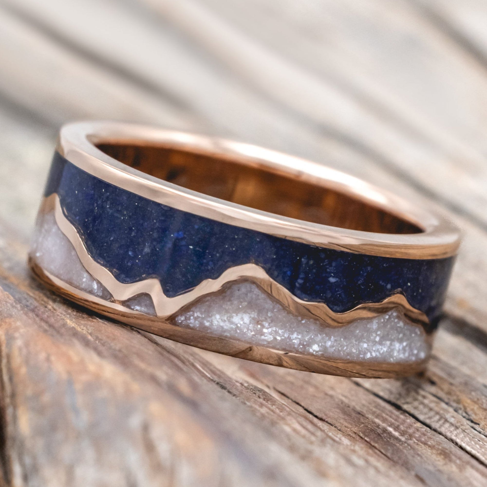 Rose gold ring with lapis lazuli and diamond dust inlay on a wooden surface