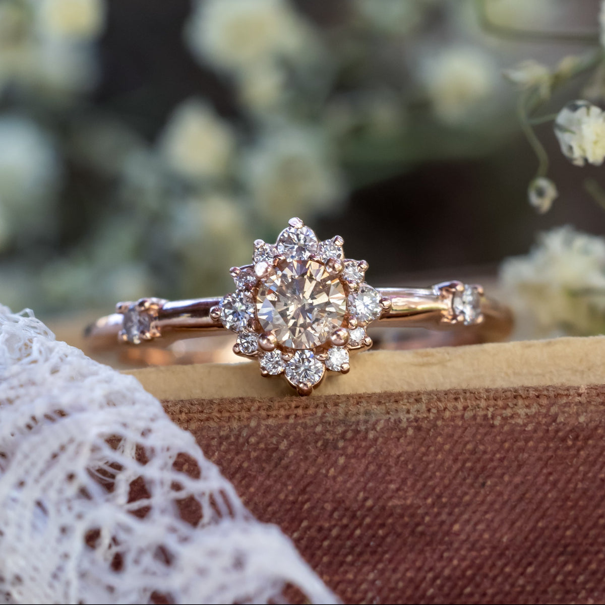 Rose gold ring with a champagne diamond and diamond halo on a decorative surface.