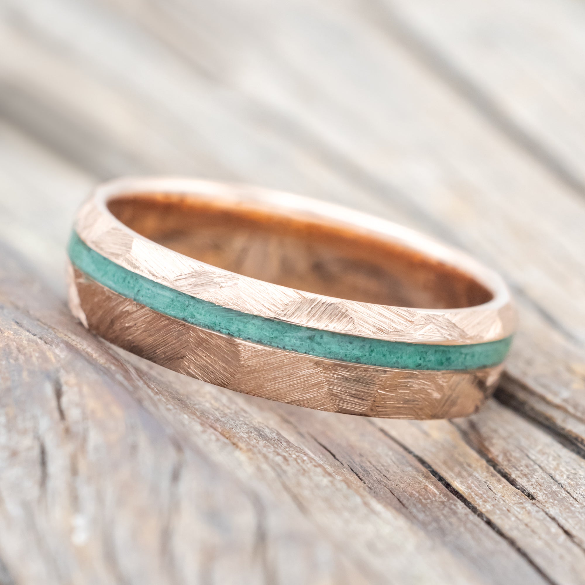 Faceted rose gold ring with malachite inlay on a wooden surface