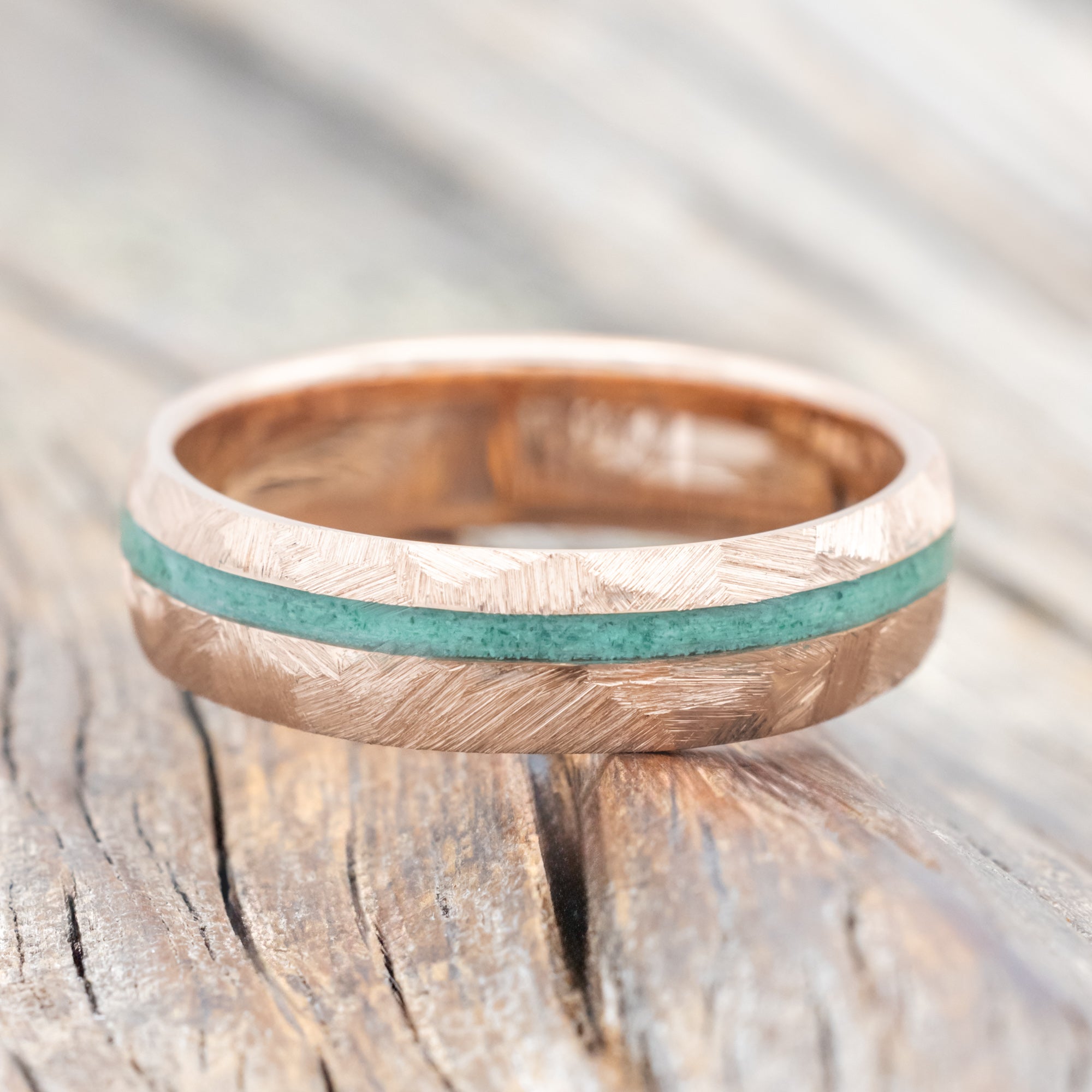 Faceted rose gold ring with malachite inlay on a wooden surface