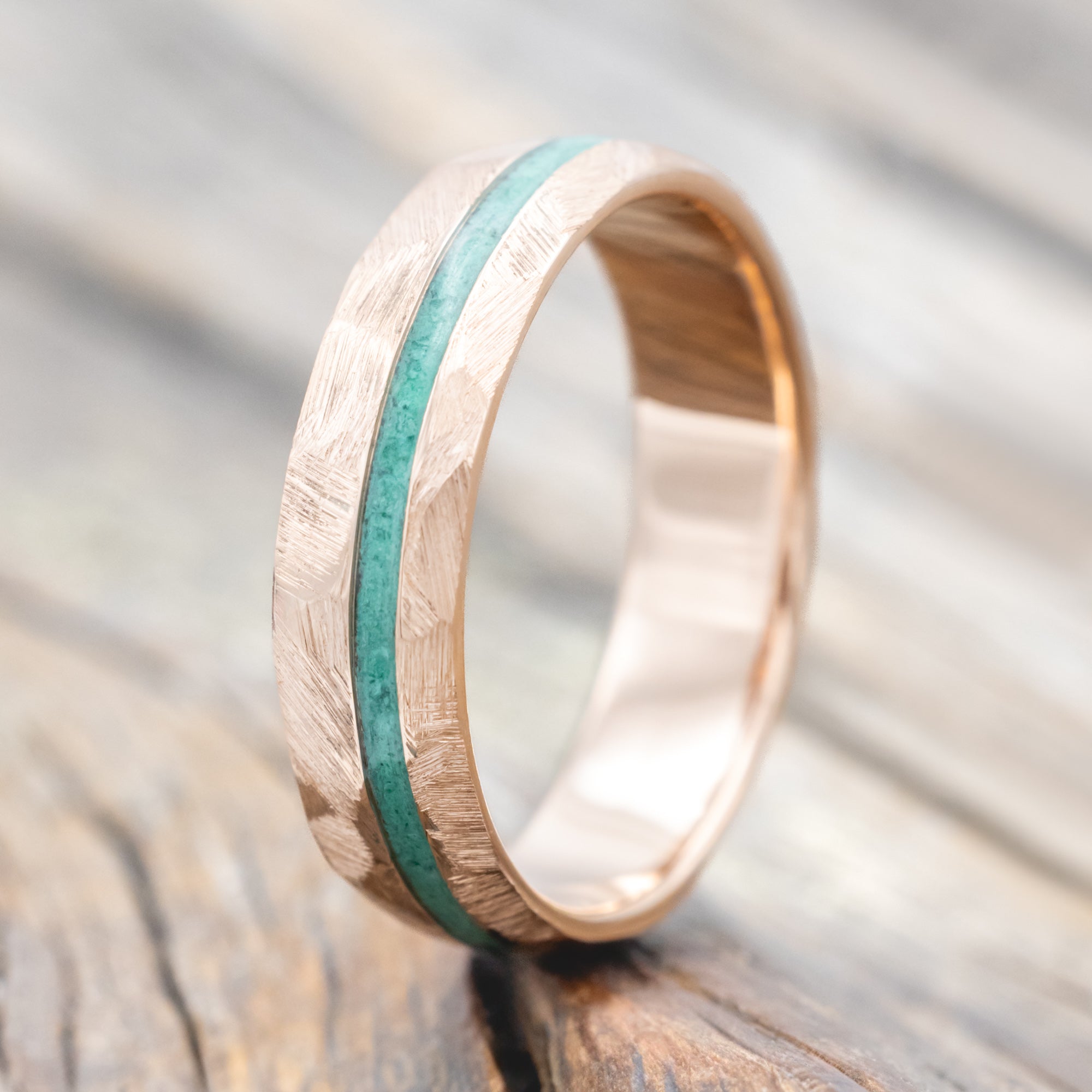 Faceted rose gold ring with malachite inlay on a wooden surface