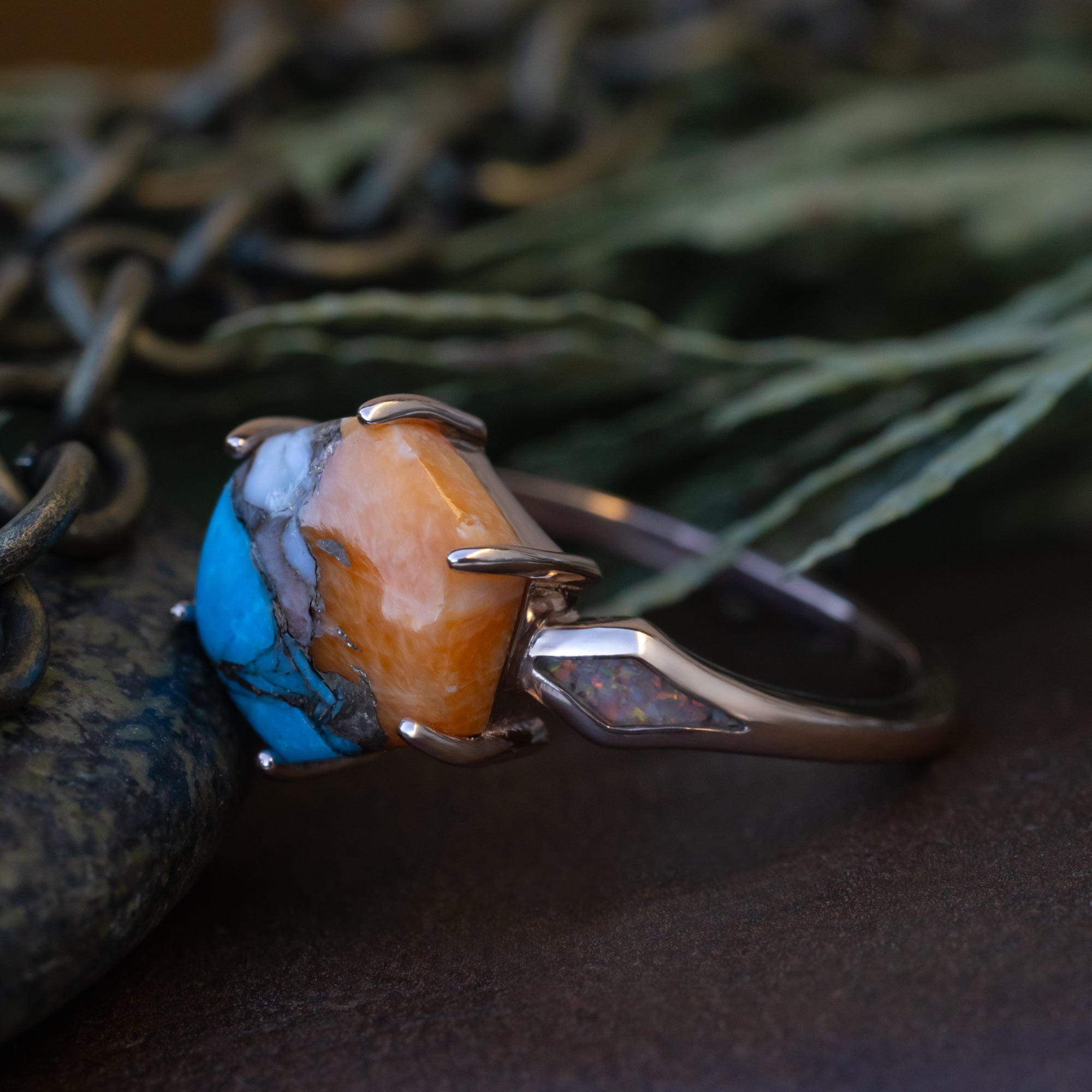 Rose gold ring with spiny turquoise on a dark surface with greenery