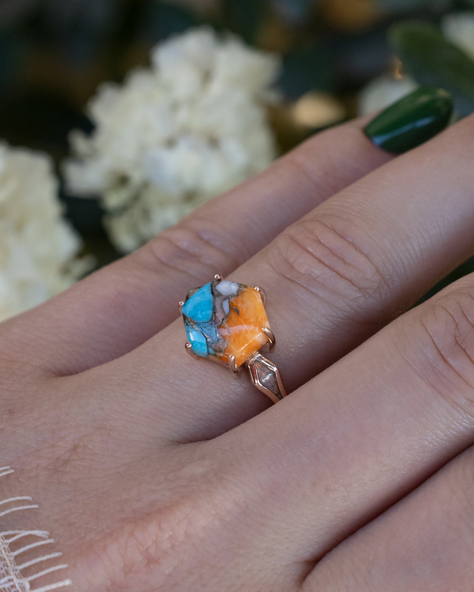 Ring with a spiny turquoise centerstone on a hand with a blurred floral background