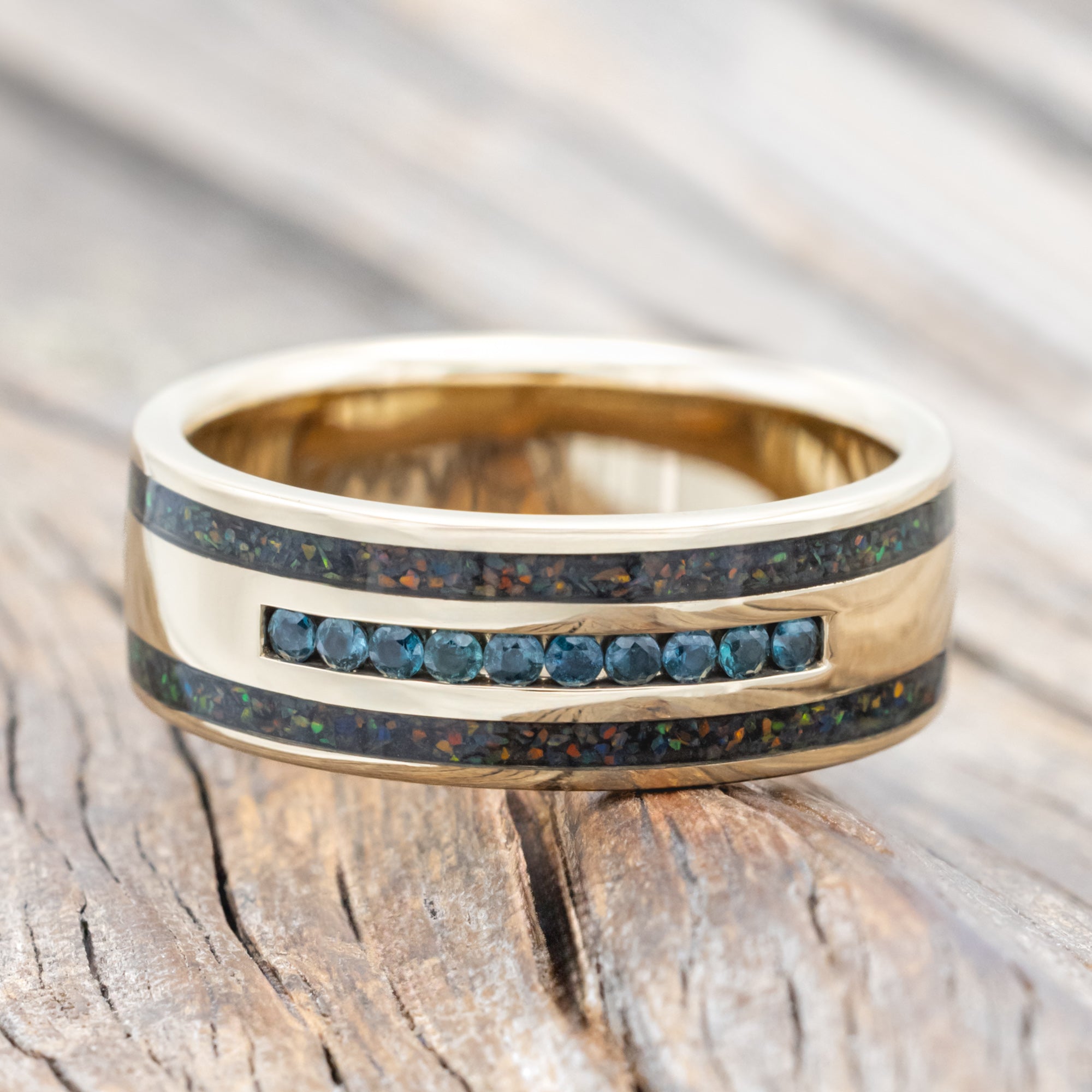 Yellow gold ring with alexandrite accents and black fire opal inlays on a wooden surface